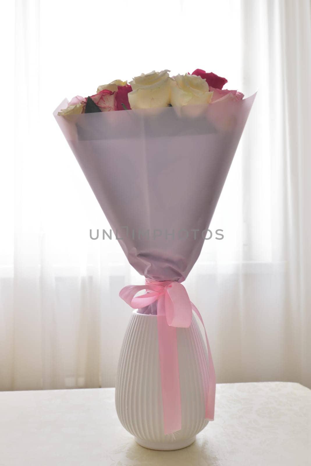 A bouquet of flowers in ceramic vase stands on a table in the room by olgavolodina