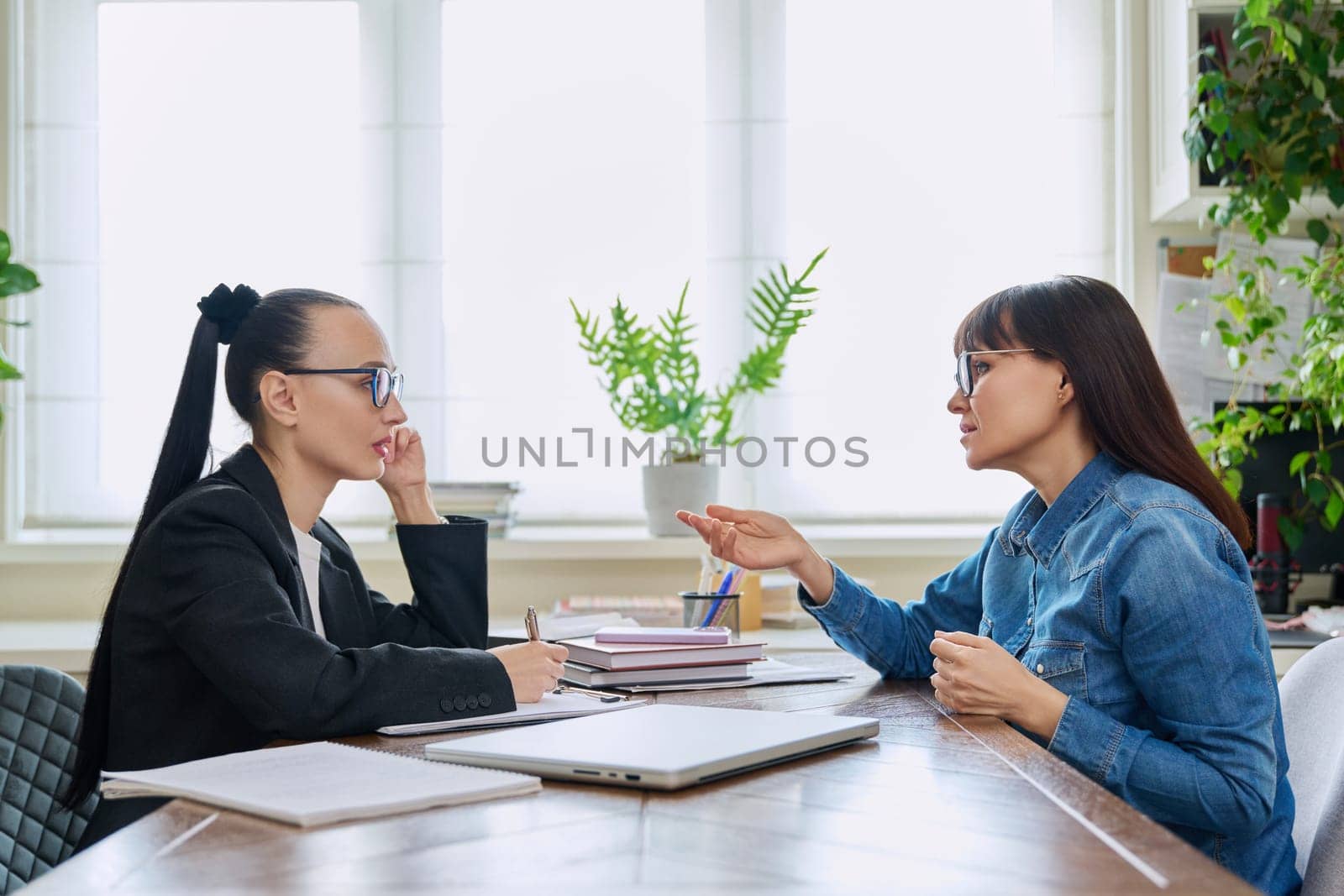 Mental therapy session of mature female with professional psychologist counselor. Talking serious women sitting at table, psychology, psychotherapy, social consultation, support, help, treatment