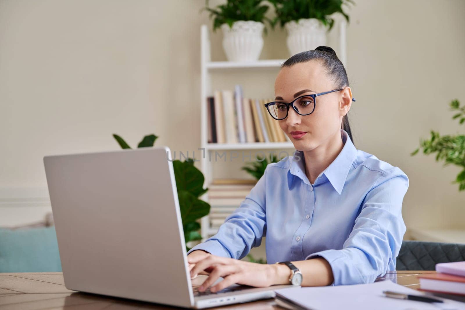 Business woman working in home office at desk with laptop computer. Serious 30s female typing looking at monitor. Remote business, technologies, internet, teaching, blogging, work, freelance concept