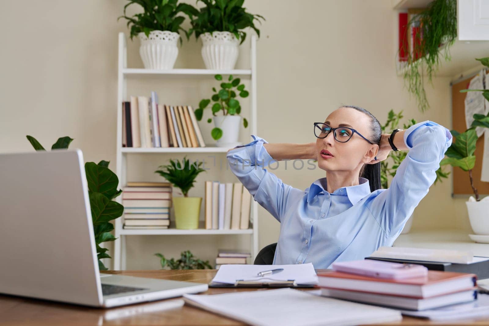 Calm relaxed business woman with her hands raised behind head in workplace, at desk with laptop computer. Tired satisfied female enjoying break, peace of mind, lack of stress