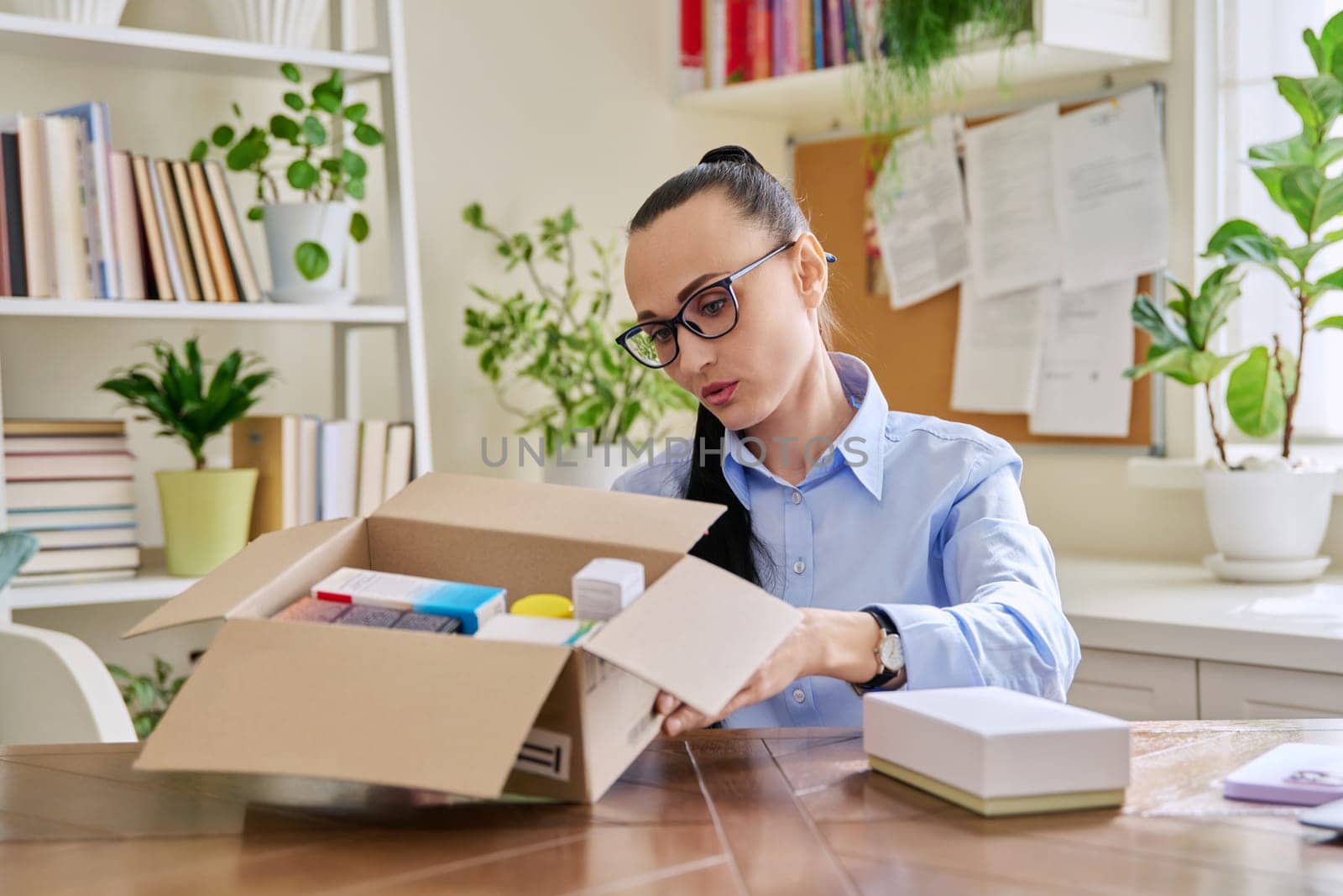 Satisfied female consumer buyer sitting at home unpacking cardboard box with online purchases. Woman unpacking boxes with cosmetics care products vitamins perfumes. Delivery by mail, online store