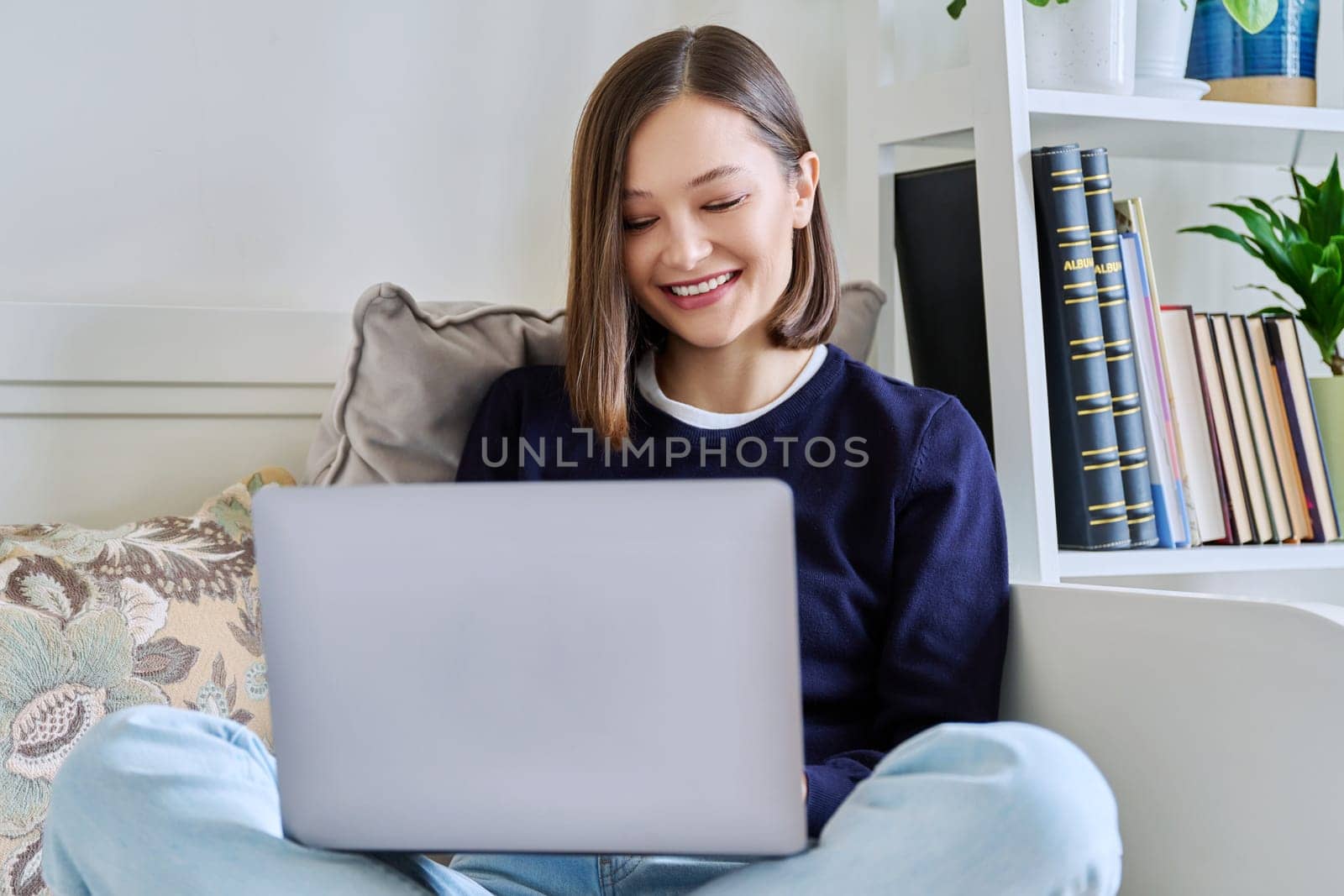 Young woman using laptop computer sitting on sofa at home. Internet online technologies for work communication study leisure