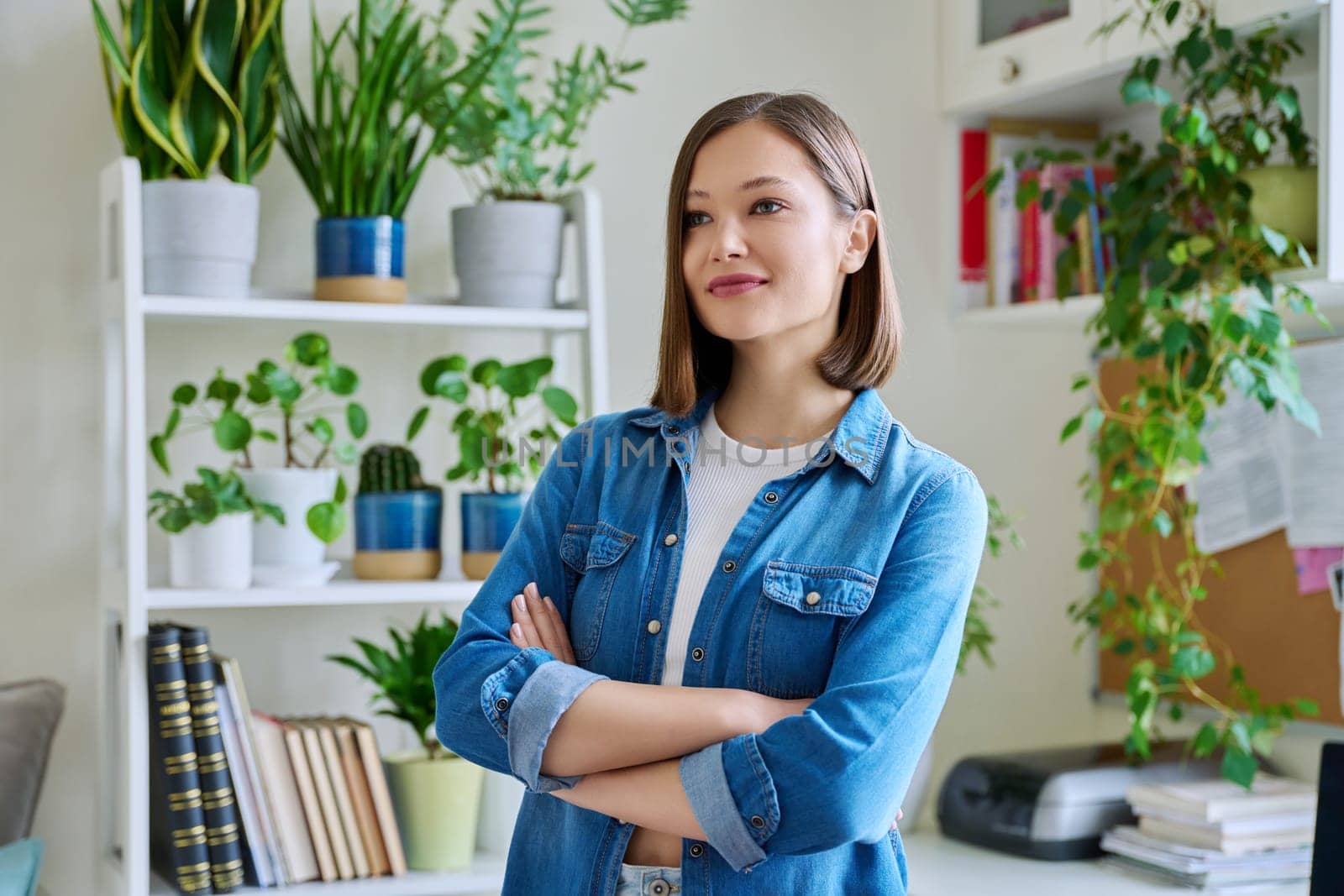 Portrait of young confident smiling woman in home interior. Beautiful positive 20s female with crossed arms. Beauty, youth, happiness, health, lifestyle concept