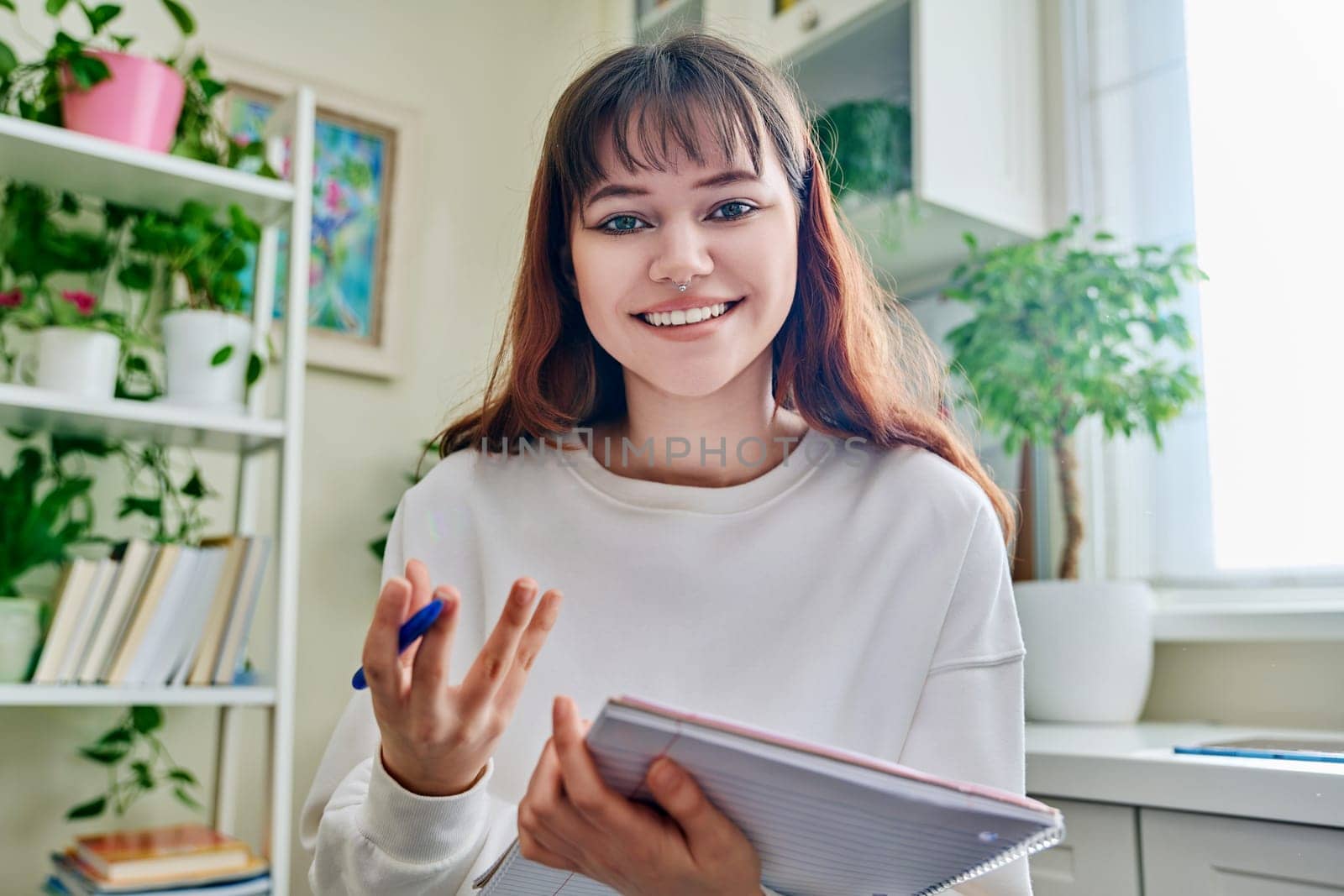 Web camera view of teenage student girl with notebook looking at camera at home. Online lesson video chat call conference. Technology education training e-learning concept