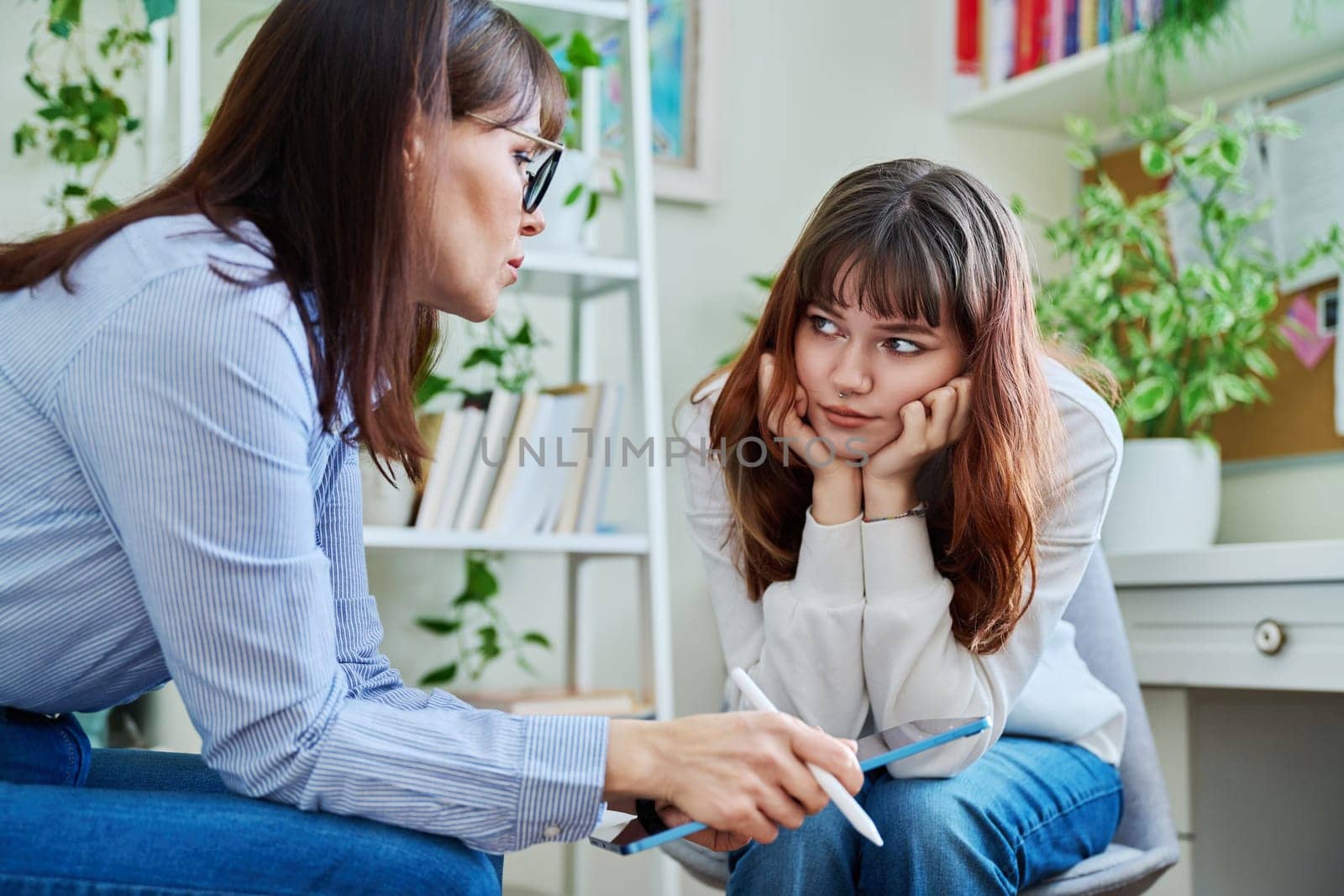 Sad, serious teenage girl at session in office of mental professional, psychologist, counselor, social worker. Feelings, difficulties, problems, depression, stress youth concept