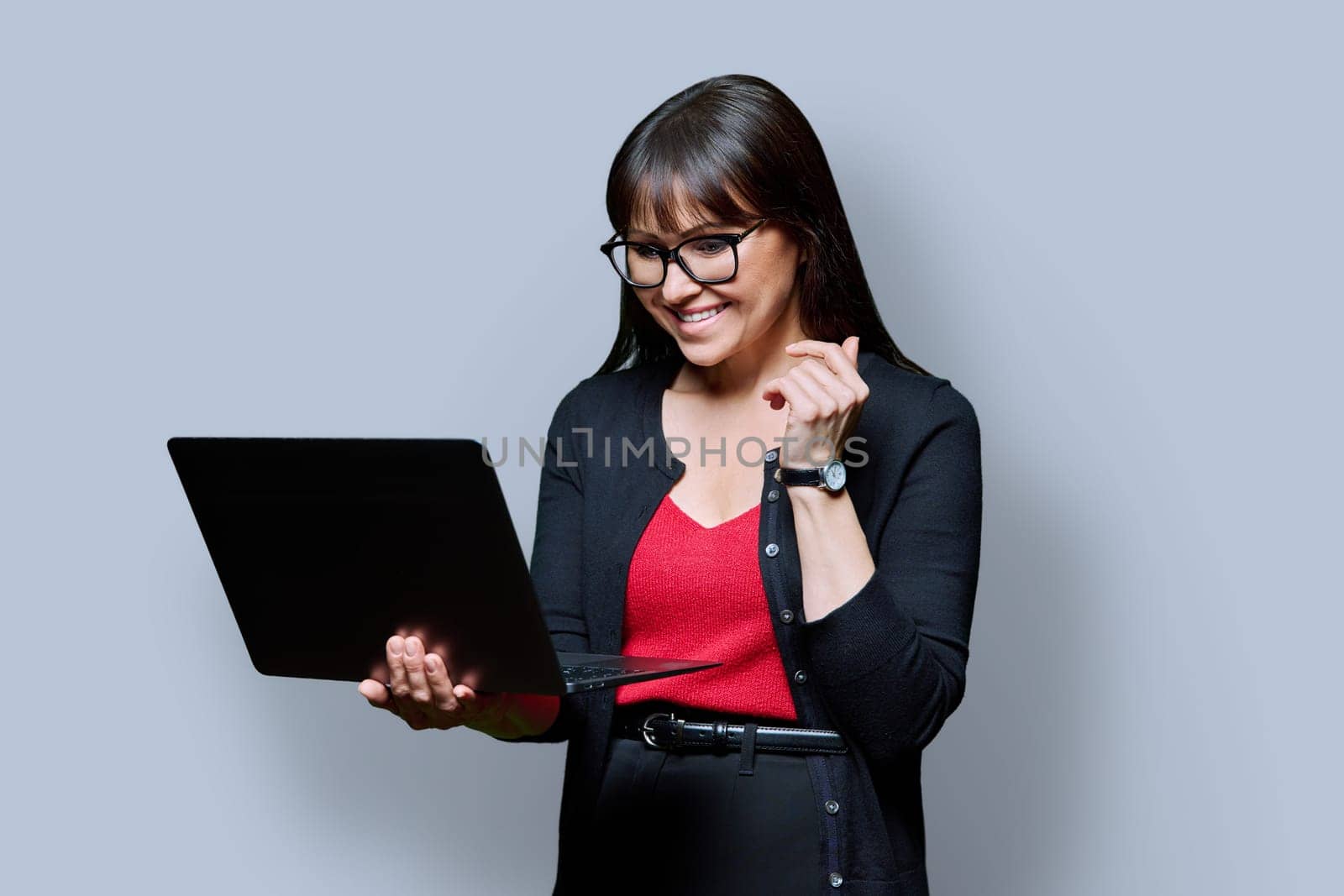 Smiling business middle aged woman using laptop on gray studio background. Confident successful mature female holding computer in hands. Business, work, job, lifestyle, technology, 40s people concept