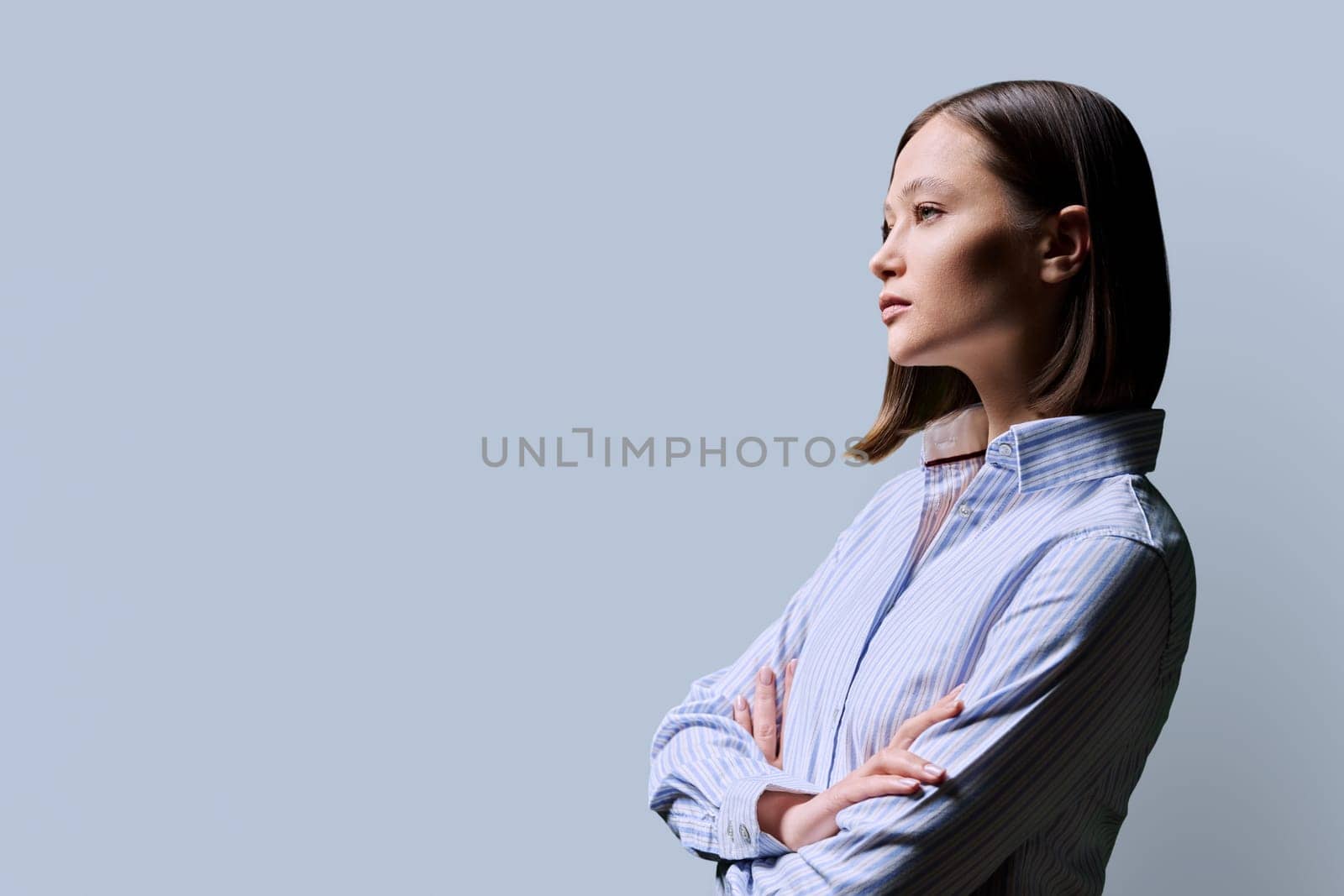 Profile view, confident serious successful young business woman with crossed arms, copy space gray studio background, space for advertising image text. Business work services education people concept