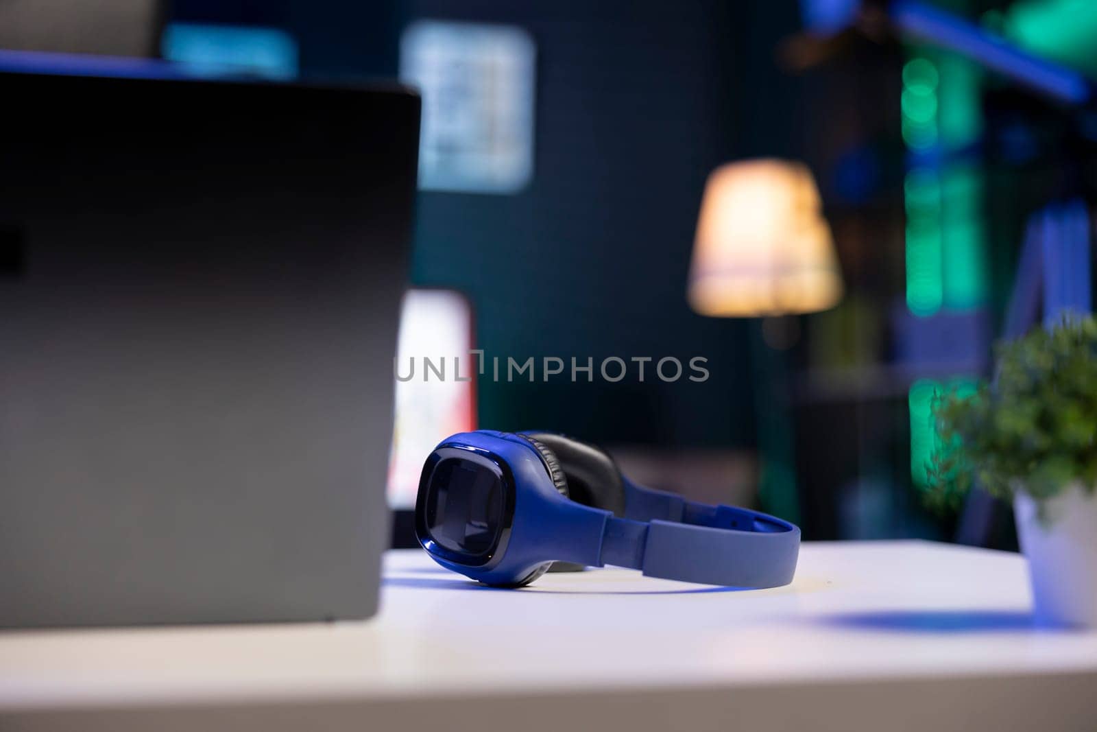 Selective focus on wireless headphones placed on a table near digital laptop. Image showing electronic devices kept on a desk for an individual to use.