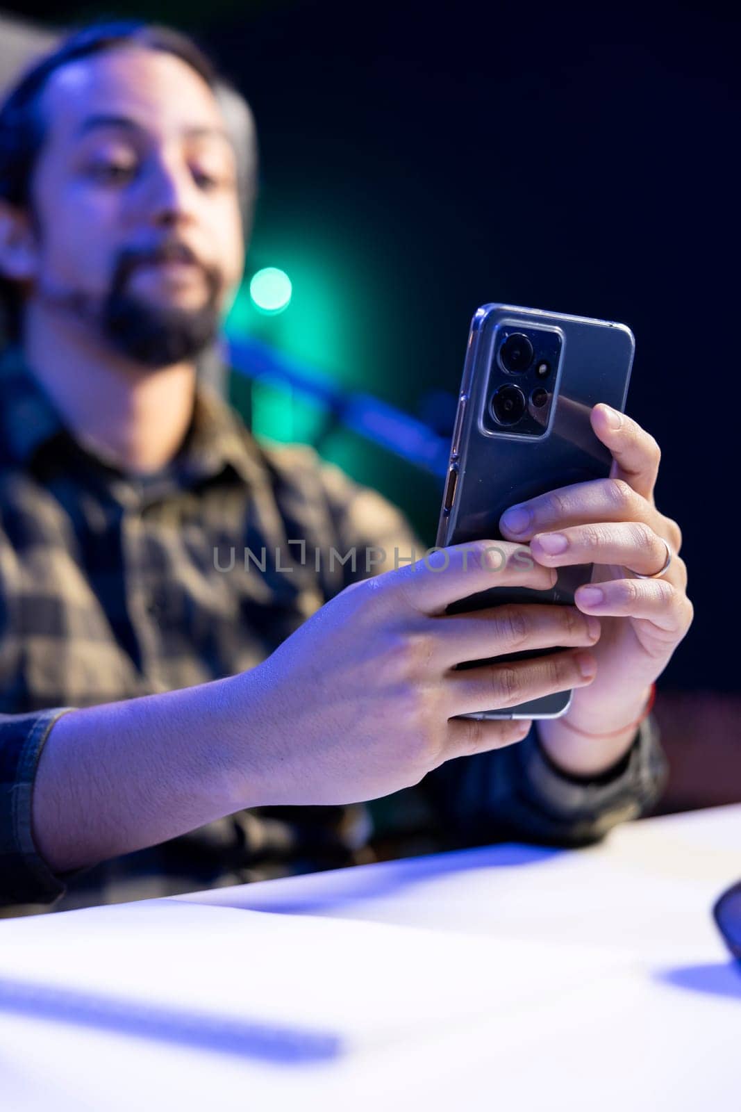 Selective focus of cell phone being held by male adult seated at the table, surfing the net and answering text messages. Young guy looking at social media platforms on his mobile device.