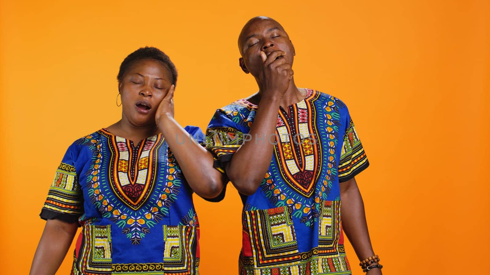 Exhausted husband and wife yawning on camera, dealing with burnout and feeling extremely tired. African american couple falling asleep standing over orange background, sleepy people.