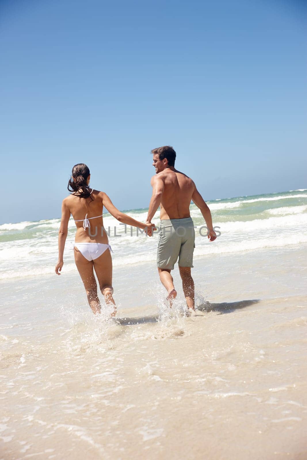 Couple, rear view and holding hands in water with travel for bonding, summer vacation and anniversary getaway. Man, woman and love by ocean with swimwear for walking, healthy relationship or blue sky by YuriArcurs