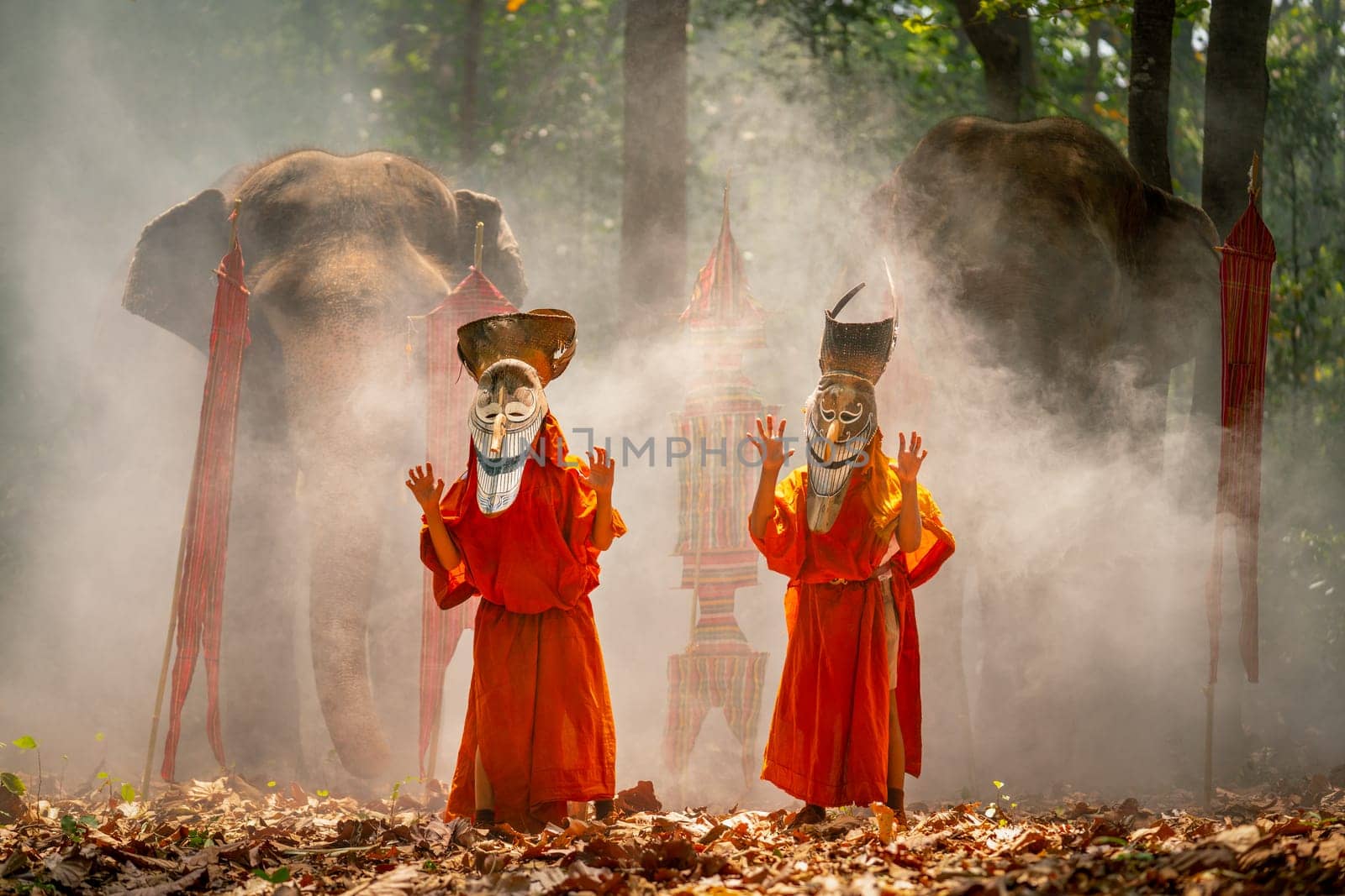 Two boy wear Pee Ta Khon, traditional culture art as ghost of Asian culture, dress and action to show horror position and elephants stand in the background and they stay in forest.