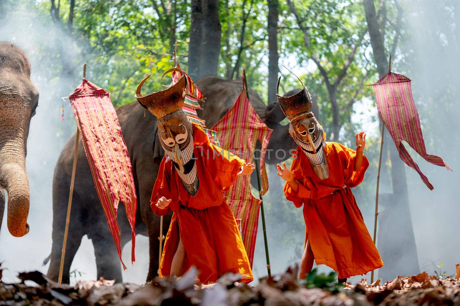 Two boy wear Pee Ta Khon, traditional culture art as ghost of Asian culture, dress and action to show horror position and elephants stand in the background also with flags.