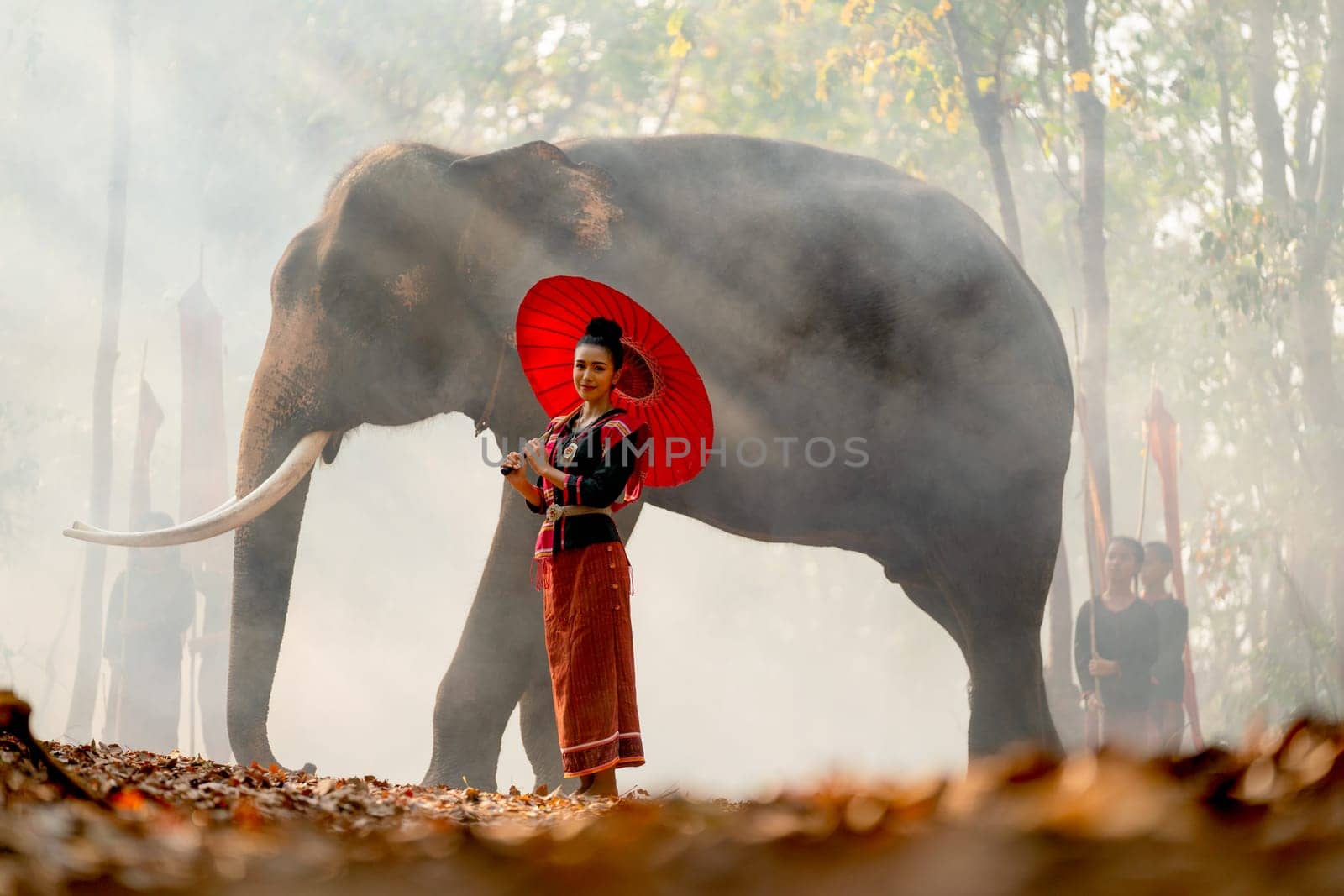 Beautiful Asian woman hold red umbrella and stand in front of big elephant and she look at camera with smiling.
