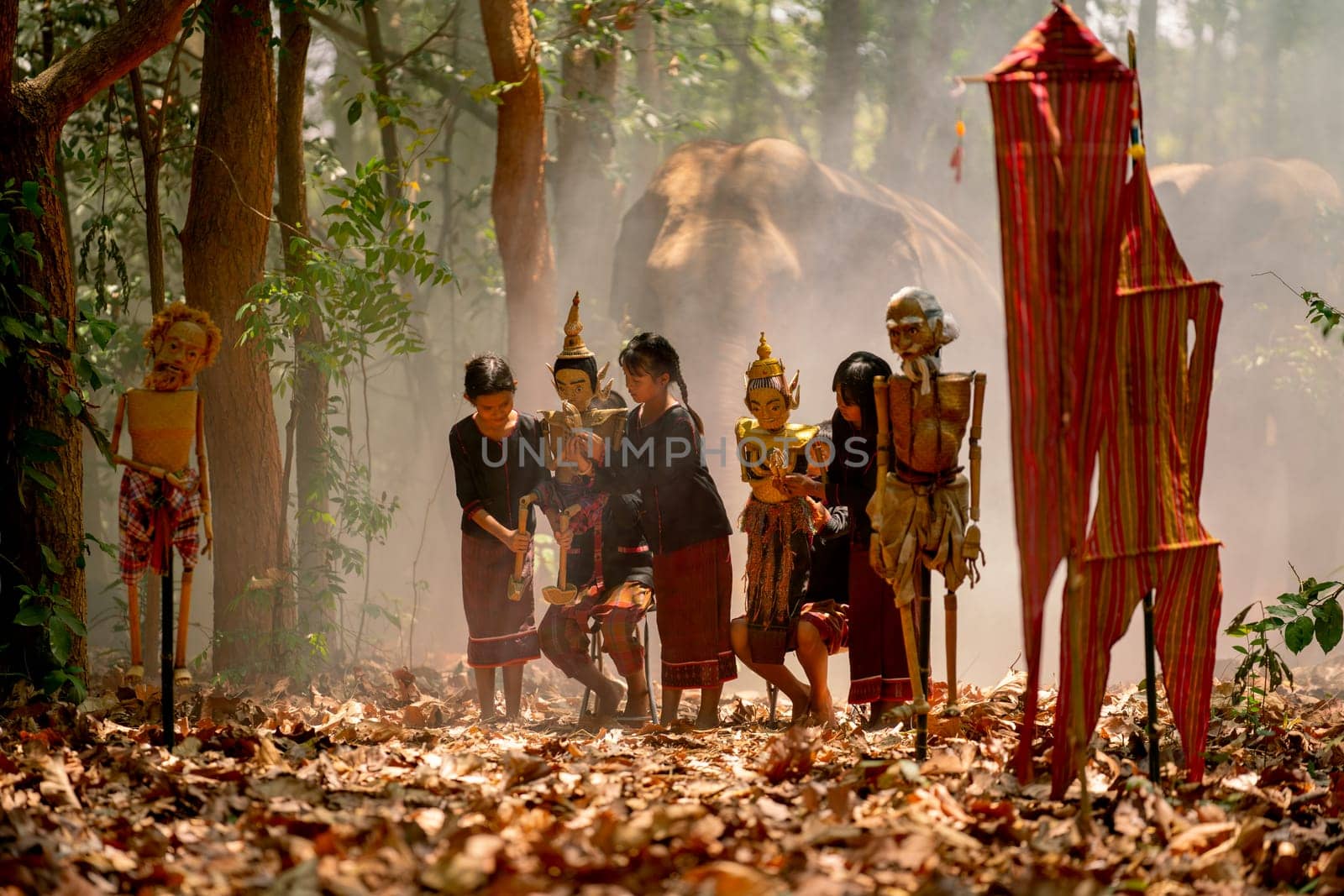 Group of Asian children show or practice manipulate the puppets in  front of big elephant in walkway in jungle and they look happy for this  traditional culture.