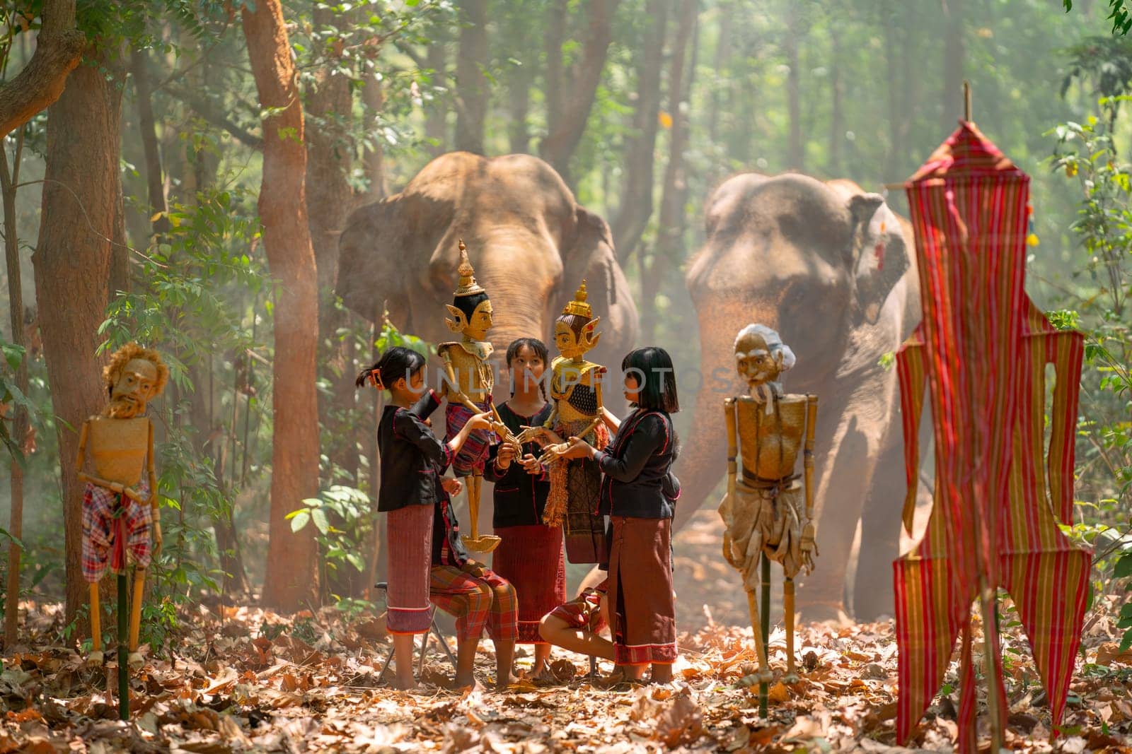 Group of Asian children enjoy to practice manipulate the puppets in  front of big elephant in walkway in jungle and they look happy for this  traditional culture.