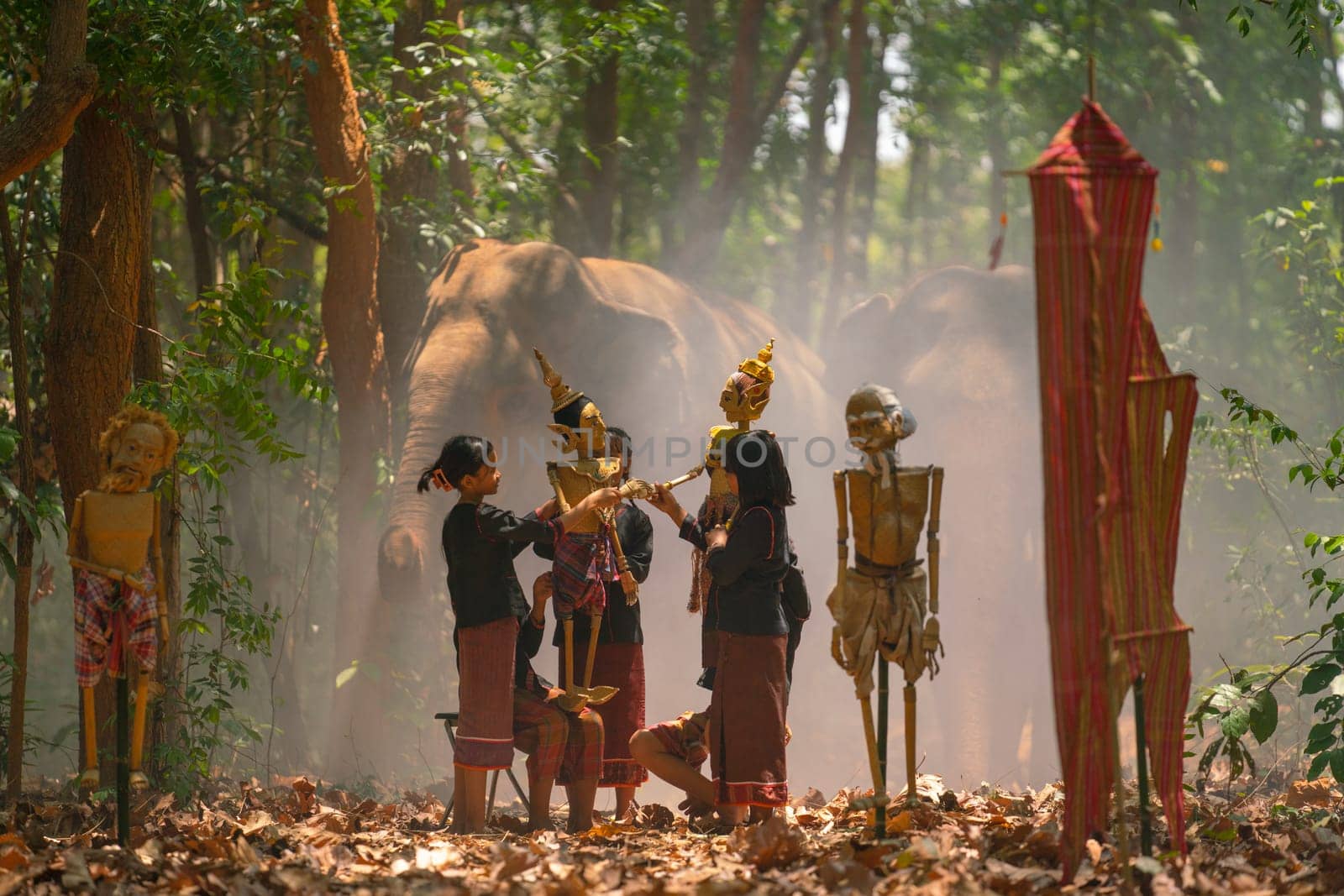 Group of Asian children show or practice manipulate the puppets in  front of big elephant in walkway in jungle and they look happy for this  traditional culture.