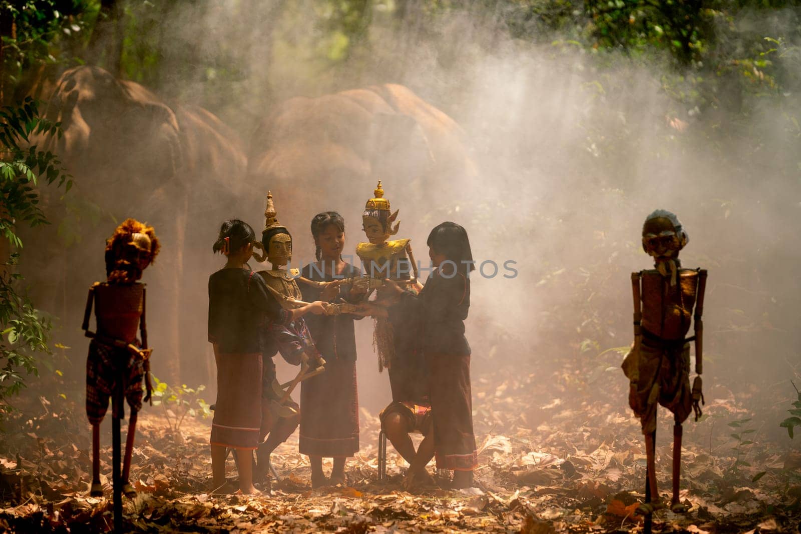Group of Asian children show or practice manipulate the puppets in  front of big elephant in walkway in jungle and they look happy for this  traditional culture.