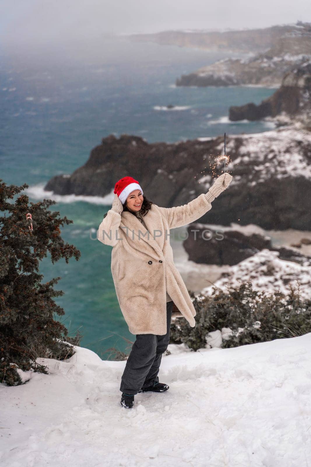 Outdoor winter portrait of happy smiling woman, light faux fur coat holding heart sparkler, posing against sea and snow background by Matiunina