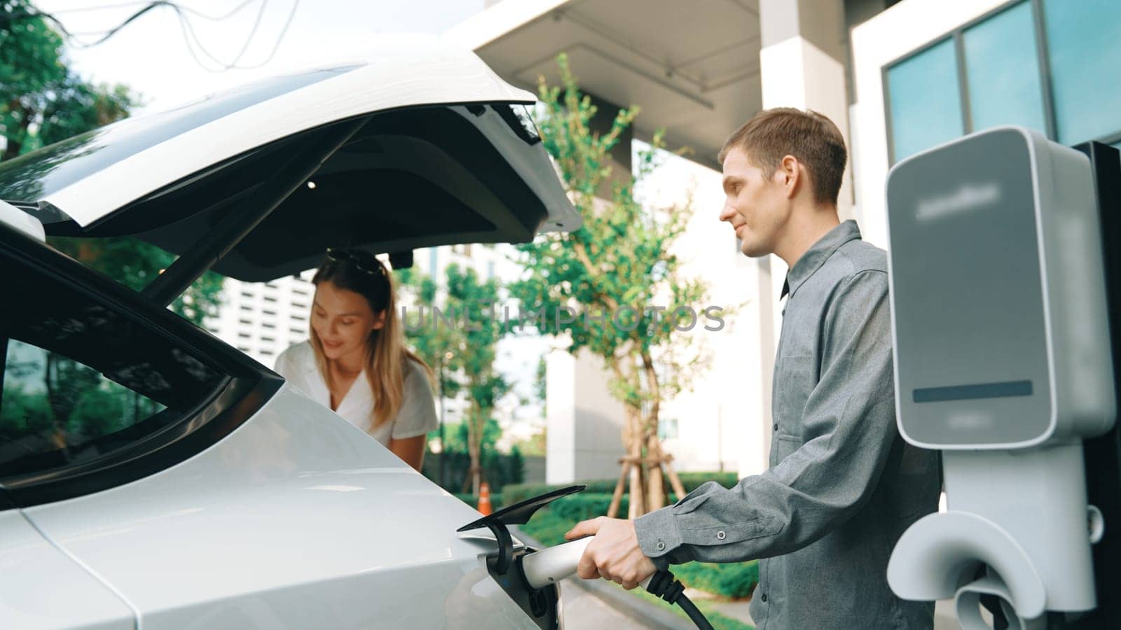 Young couple travel with EV electric car in green sustainable city innards by biancoblue