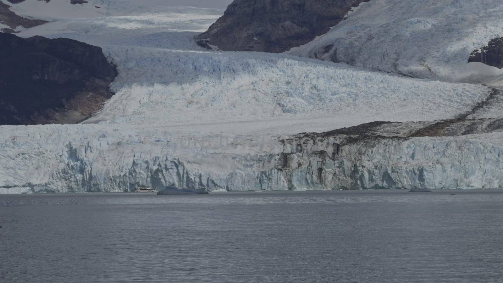 Tourists on a boat observe the immense Spegazzini Glacier in Argentina, appreciating the grandeur of nature.