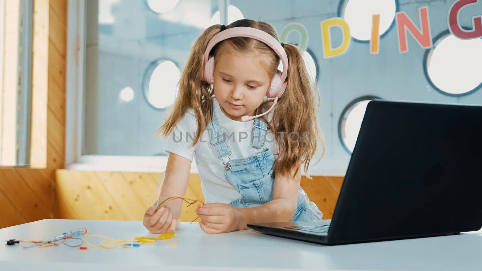 Pretty girl wearing headphone while study electronic equipment. Caucasian child doing science experiment while laptop, screwdriver and wires placed near on table. Smart online classroom. Erudition.