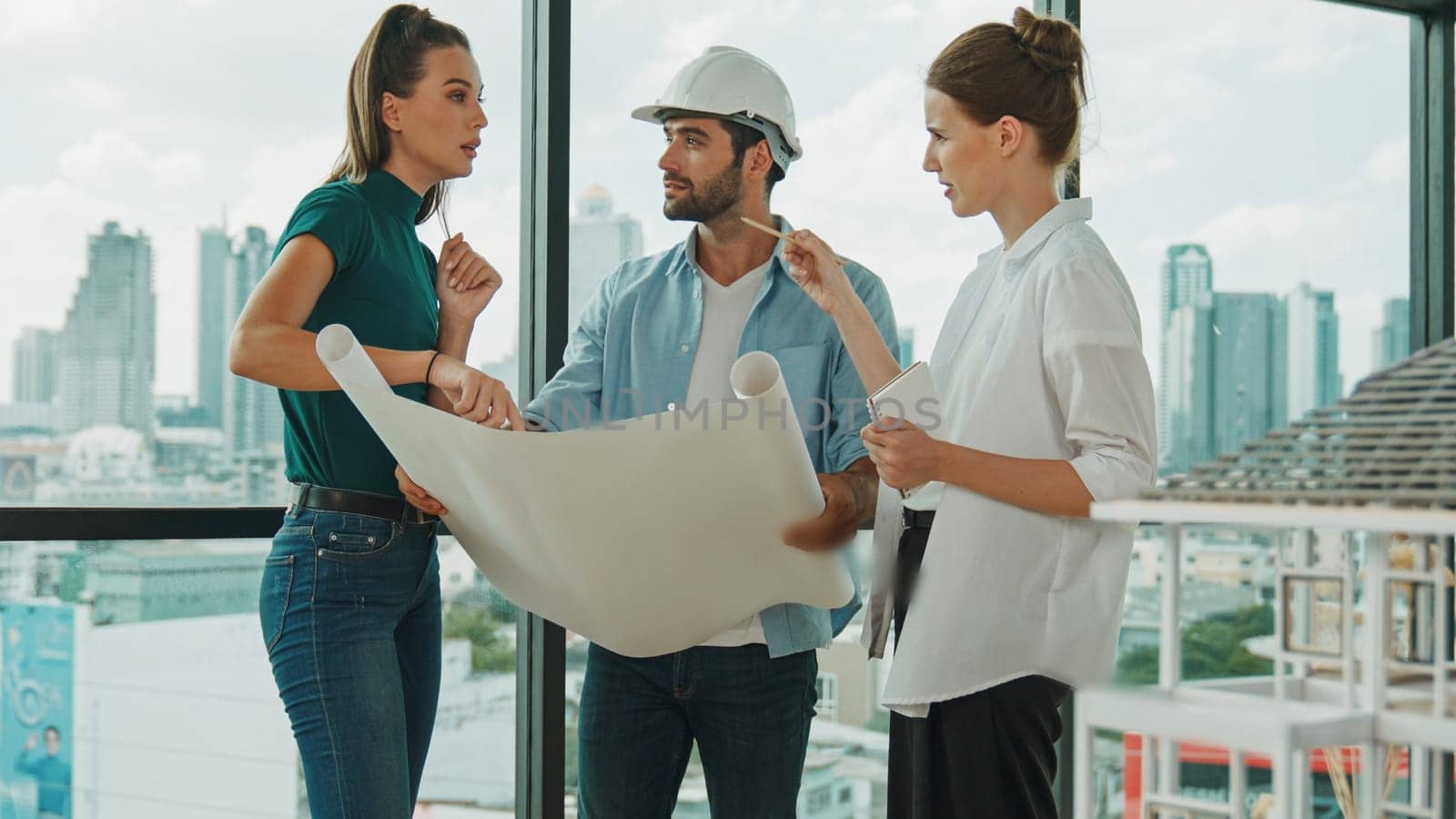 Professional architect engineer team talking, sharing, brainstorming about design while manager hold at project plan. Young architect holding plan while manager listen and point at plan. Tracery