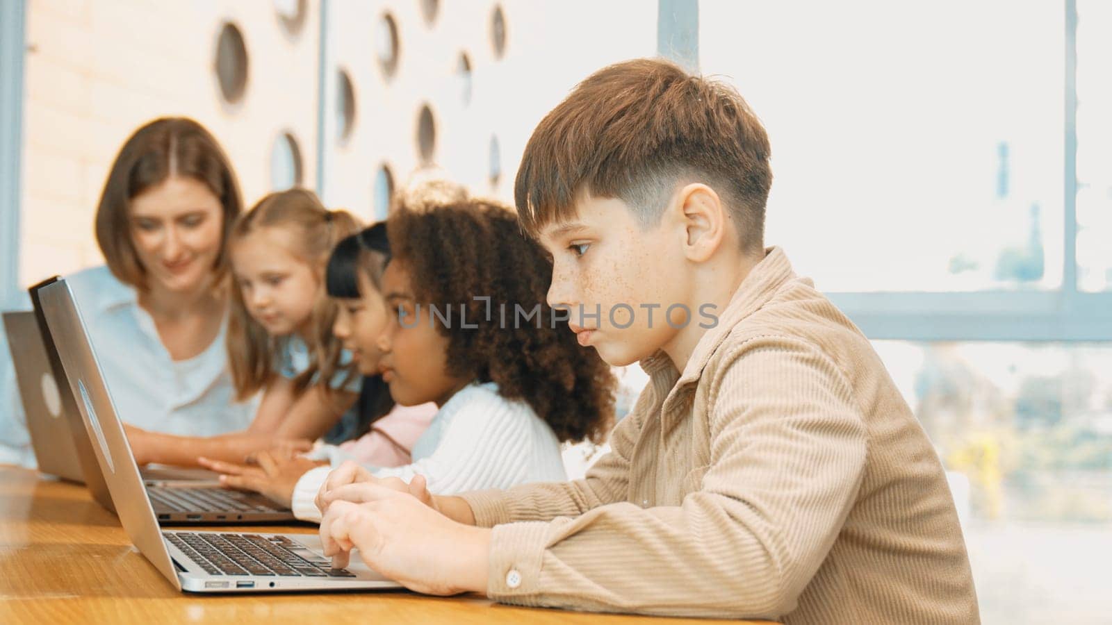 Boy playing laptop with multicultural friend learning prompt at STEM technology class. Multicultural student study about engineering code and programing system with blurring background. Erudition.