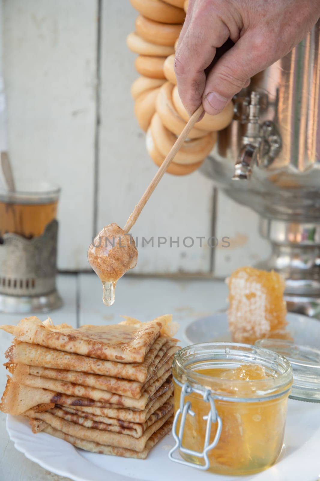 A man pours honey on pancakes and drinks tea from a samovar, Russian tradition of celebrating Maslenitsa. High quality photo