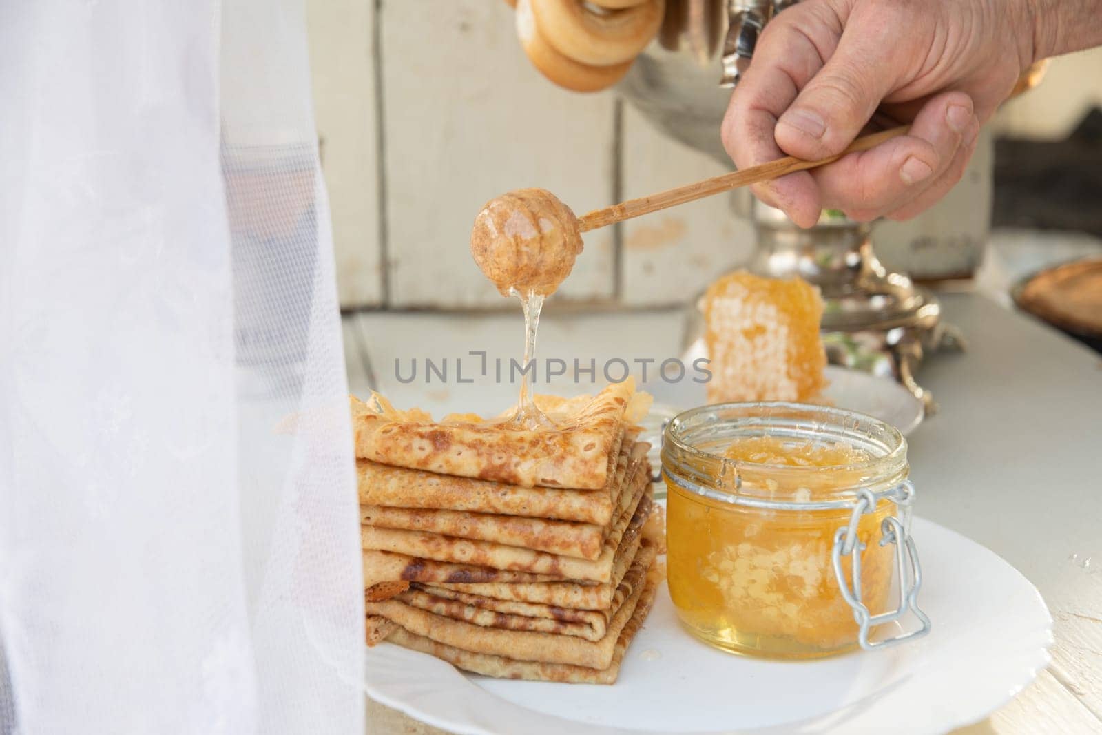 A man pours honey on pancakes and drinks tea from a samovar, Russian tradition of celebrating Maslenitsa by KaterinaDalemans