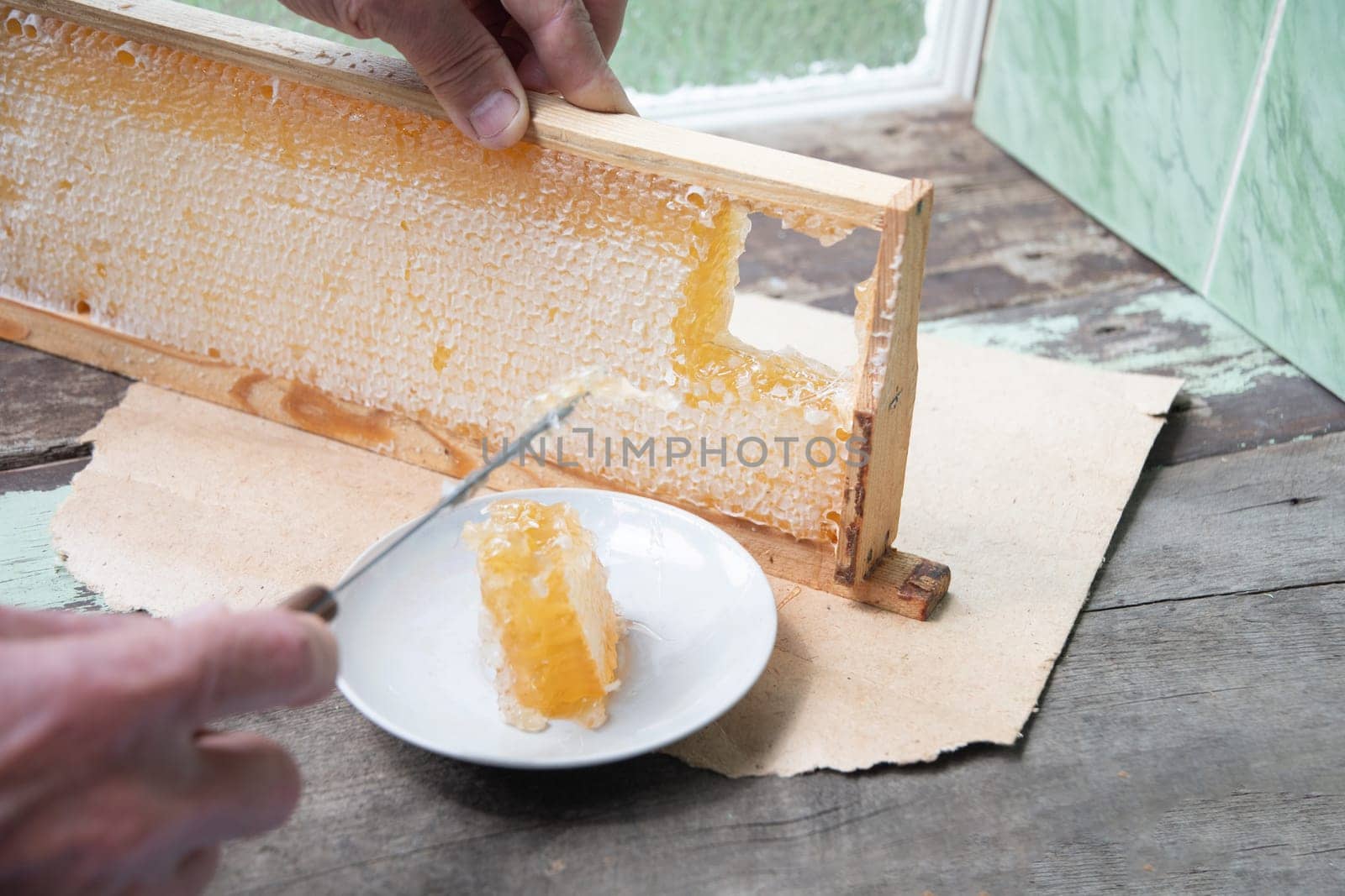 man cuts honeycombs from a honey frame with a knife for eating for tea, honey in honeycombs is good for the health by KaterinaDalemans