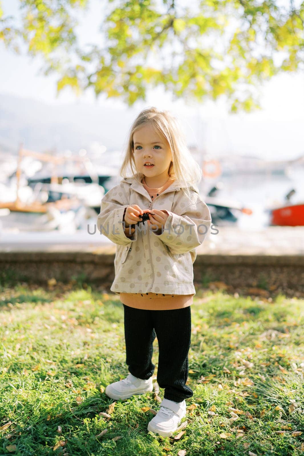 Little smiling girl stands on a green flowerbed on the embankment. High quality photo