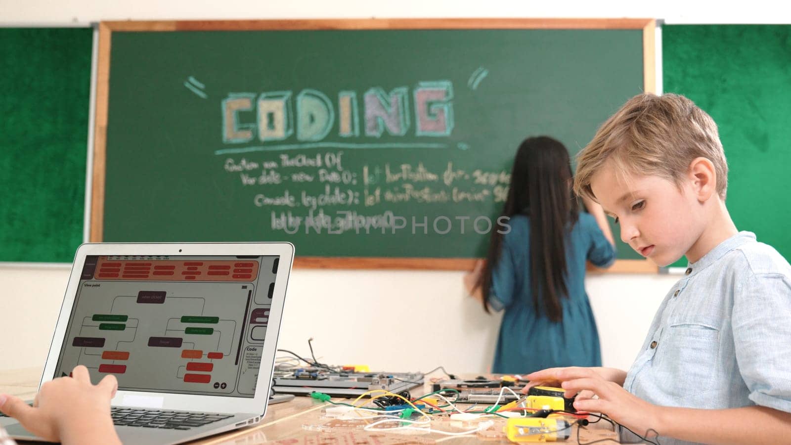 Asian boy coding program while caucasian friend fixing electric board at STEM class. Energetic student standing blackboard while writing coding engineering prompt and programing AI software. Pedagogy.