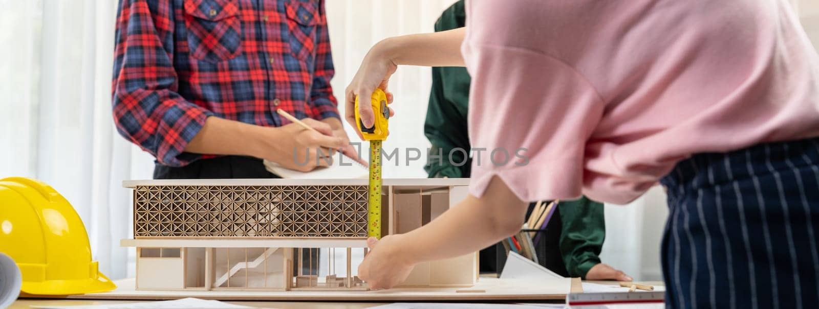 Smart architect engineer and interior designer working together and measuring house model by using ruler on meeting table with blueprint and architectural equipment. Teamwork concept. Burgeoning.