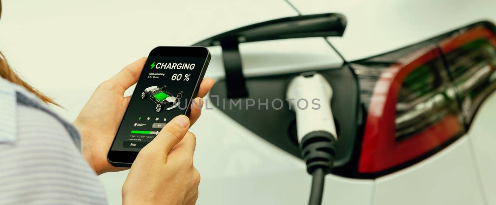 Young woman using smartphone online banking application to pay for electric car battery charging from EV charging station during vacation holiday road trip at national park or forest. Panorama Exalt