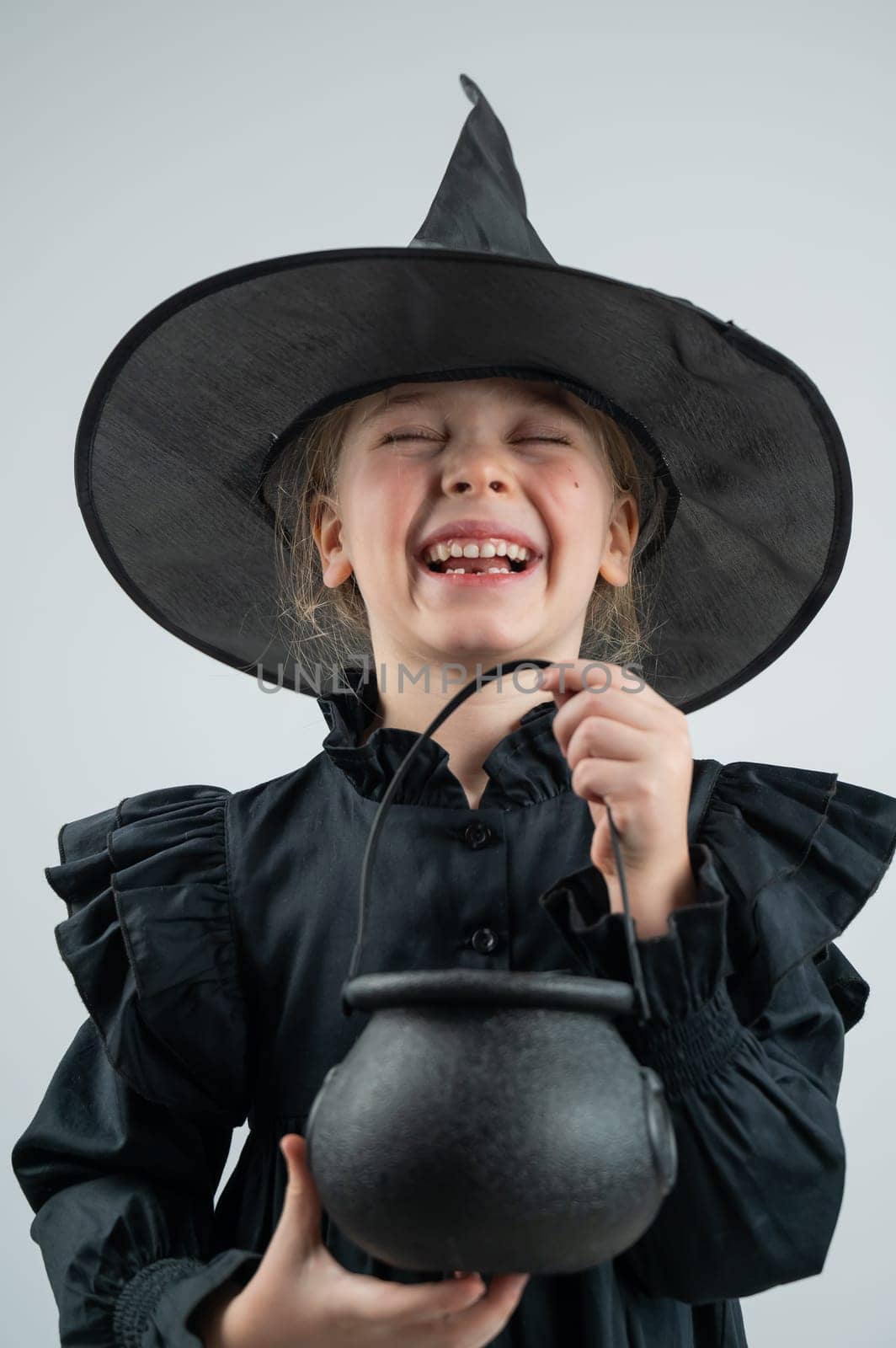 Portrait of a little Caucasian girl in a witch costume holding a cauldron on a white background. Vertical photo. by mrwed54