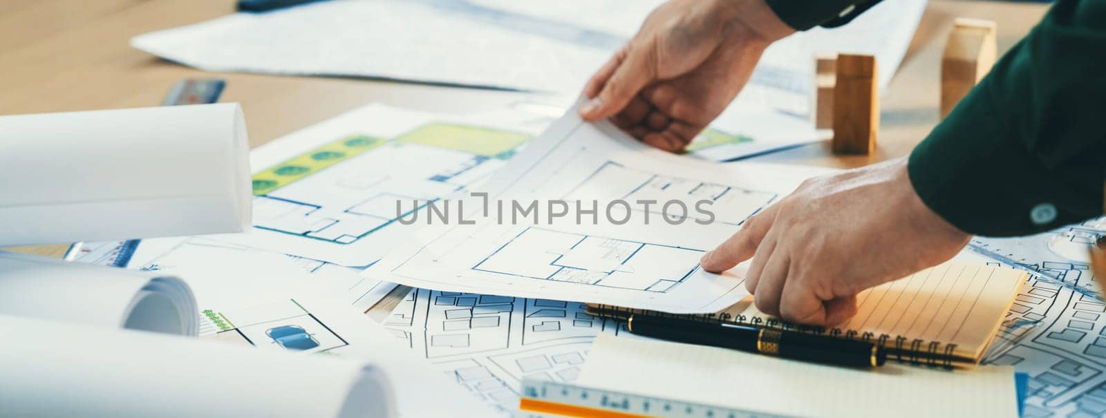 A portrait of experienced male architect 's hand chooses the blueprint on messy table with architectural project and wooden block scattered around. Business and environment concept. Delineation.