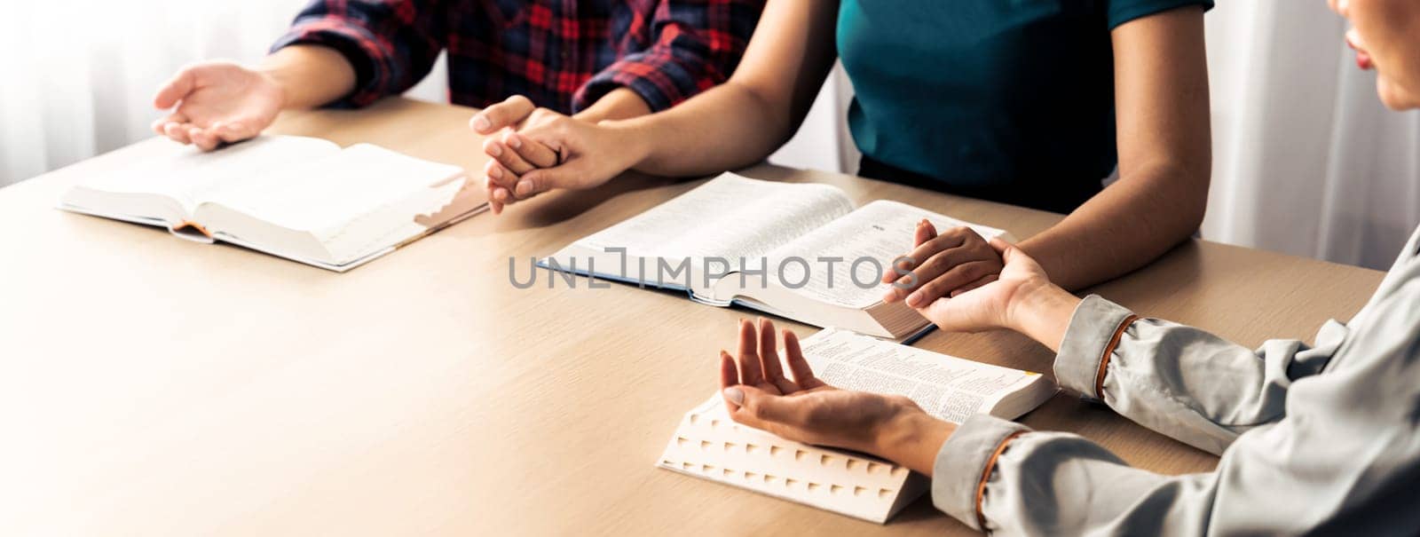 Cropped image of diversity people hand praying together at wooden church on bible book. Group of believer hold hand together faithfully. Concept of hope, religion, faith, god blessing. Burgeoning.