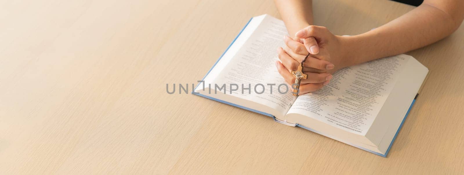 Cropped image of praying male hand holding cross on holy bible book at wooden table. Top view. Concept of hope, religion, faith, christianity and god blessing. Warm and brown background Burgeoning.