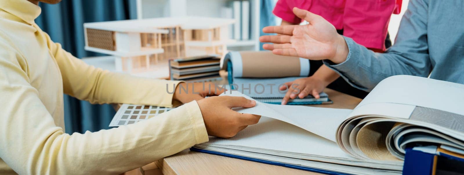 Skilled interior design team carefully selecting curtain materials while coworker selecting the color of curtain with house model placed on meeting table. Creative design concept. Variegated.