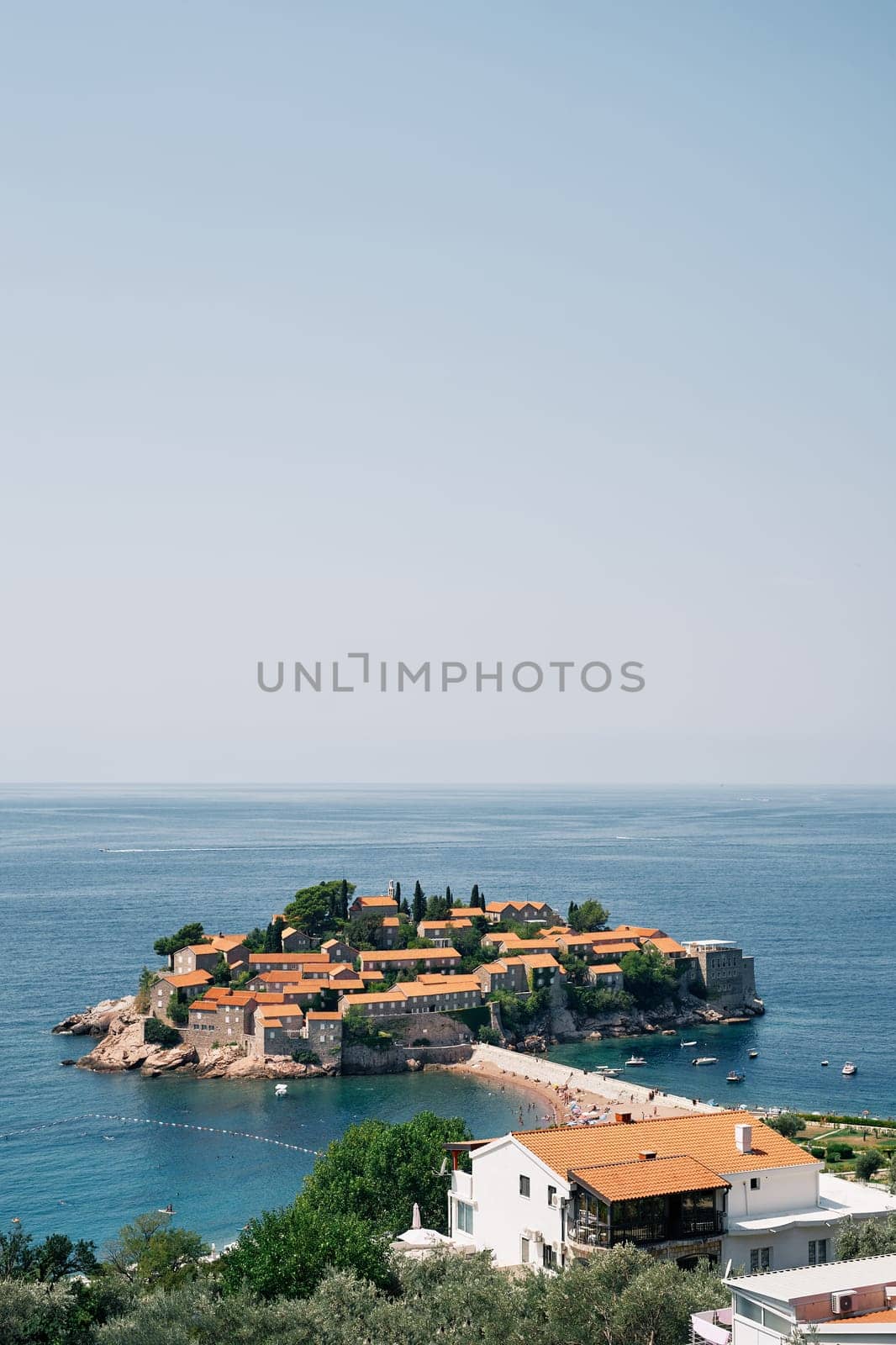 View over the red roofs of old houses to the island of Sveti Stefan. Montenegro by Nadtochiy