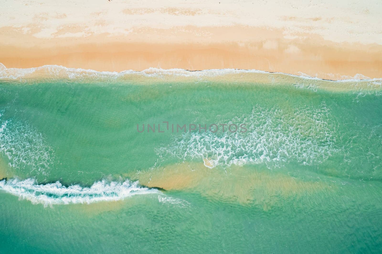 Aerial view of sandy beach and turquoise ocean. Top view of ocean waves reaching shore on sunny day. by Busker