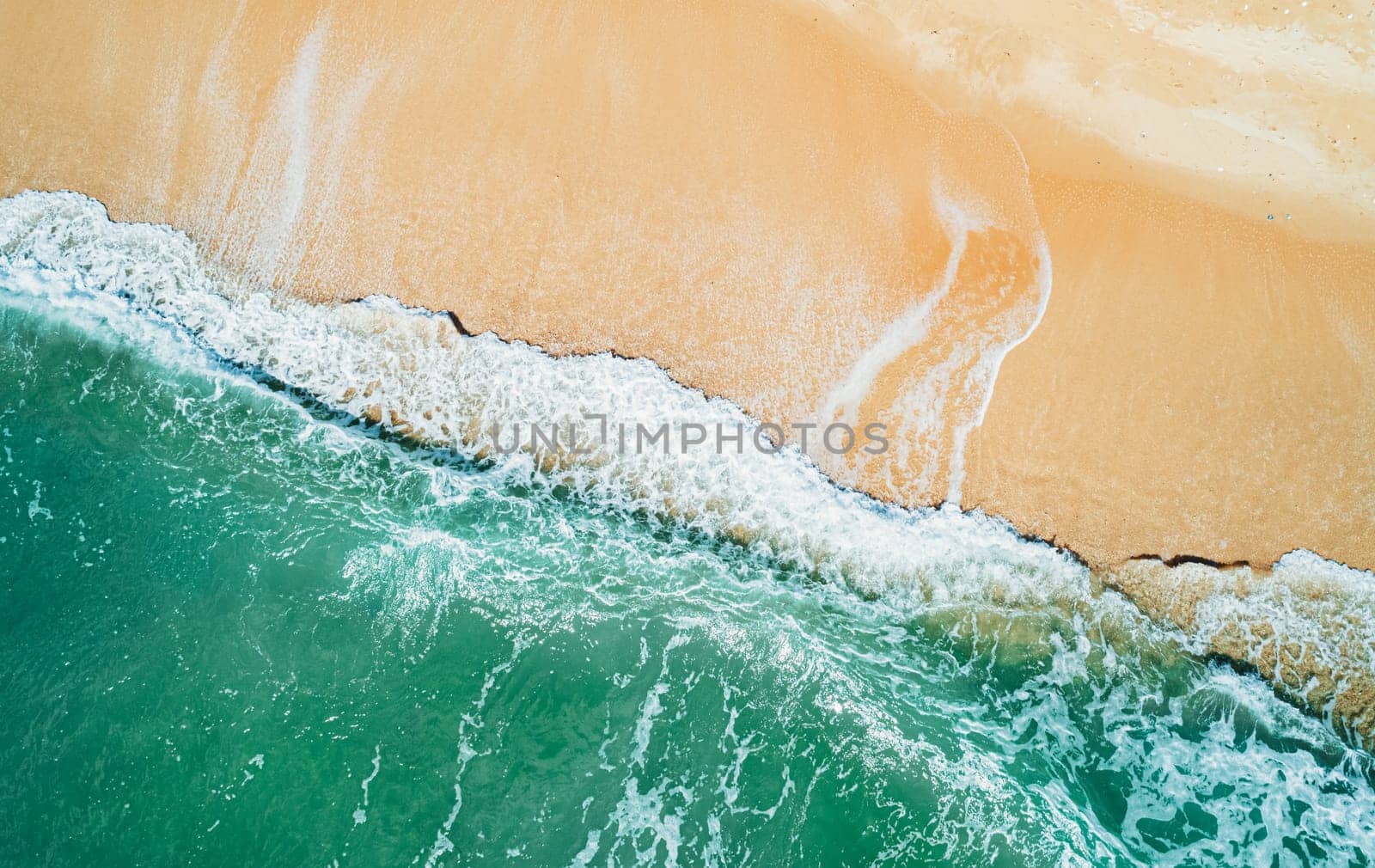 Aerial top down view of turquoise ocean wave reaching the coastline.