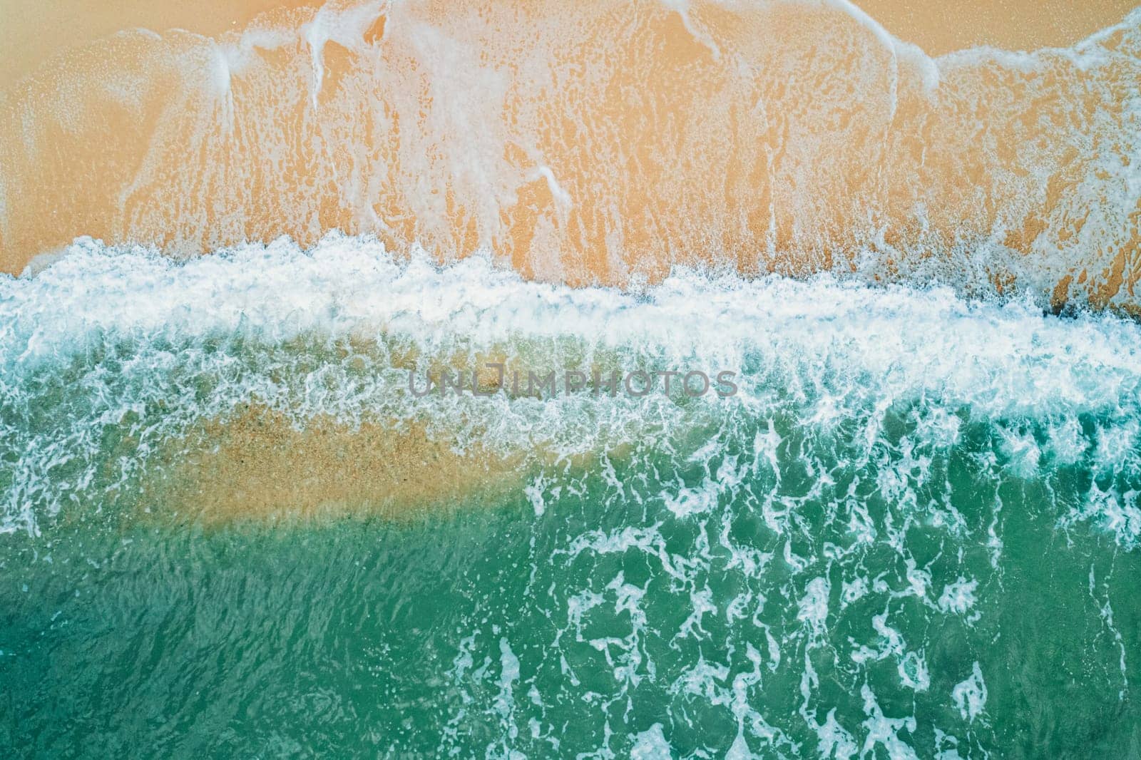 Aerial top down view of turquoise ocean wave reaching the coastline.