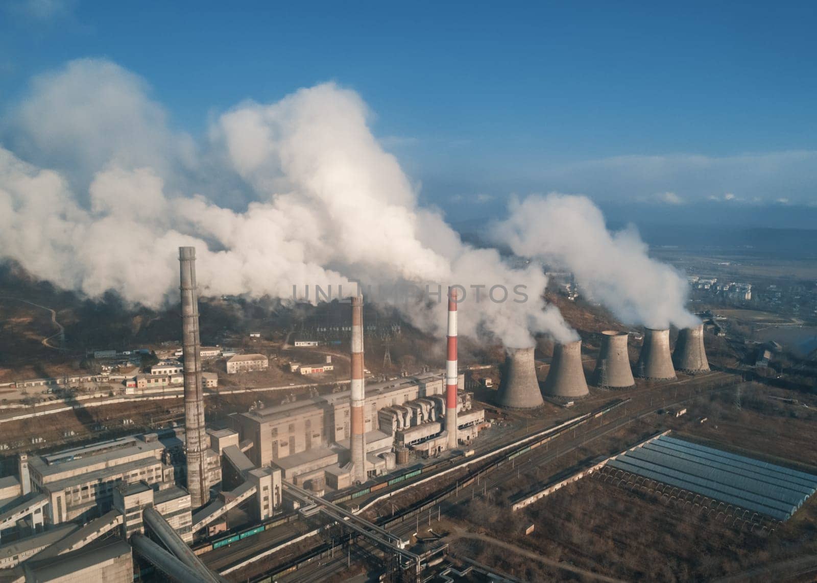 Aerial view of tall chimney pipes with grey smoke from coal power plant. Production of electricity with fossil fuel. Ecology and pollution of nature. by Busker