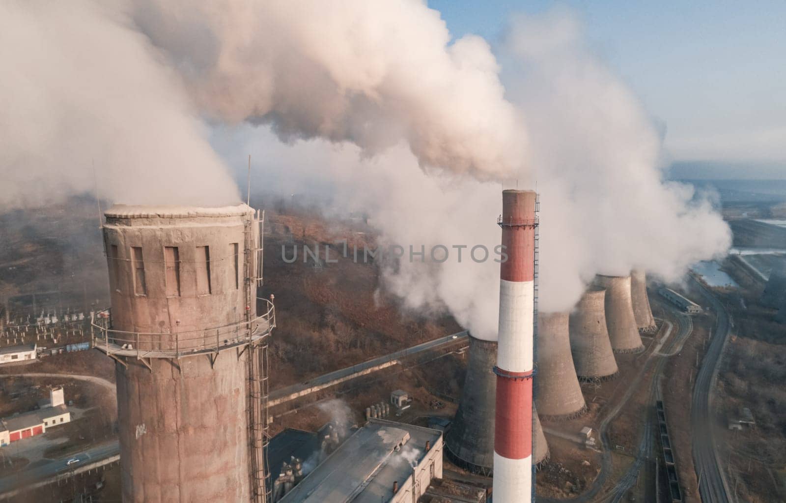 Aerial view of tall chimney pipes with grey smoke from coal power plant. Production of electricity with fossil fuel. Ecology and pollution of nature. by Busker