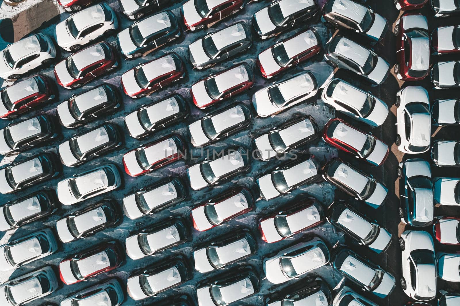 Aerial top down view of new cars parked in car parking lot. Car dealer parking lot full of new automobiles. New cars lined up for import and export business.