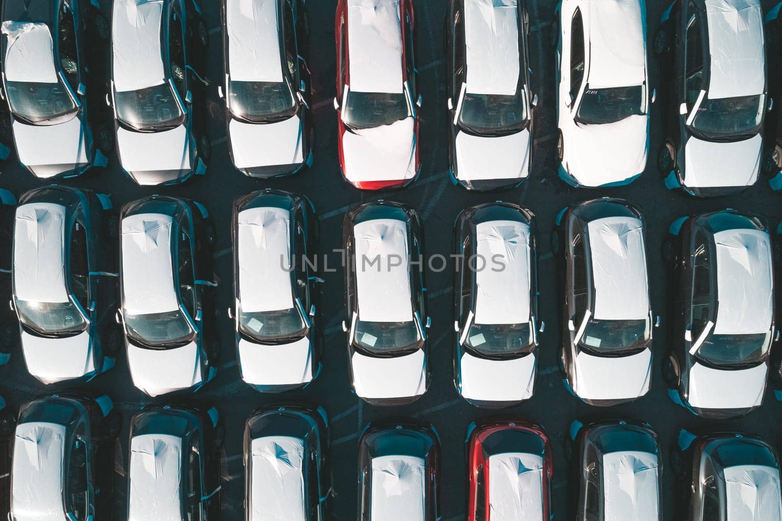 Aerial top down view of new cars parked in car parking lot. Car dealer parking lot full of new automobiles. New cars lined up for import and export business. by Busker