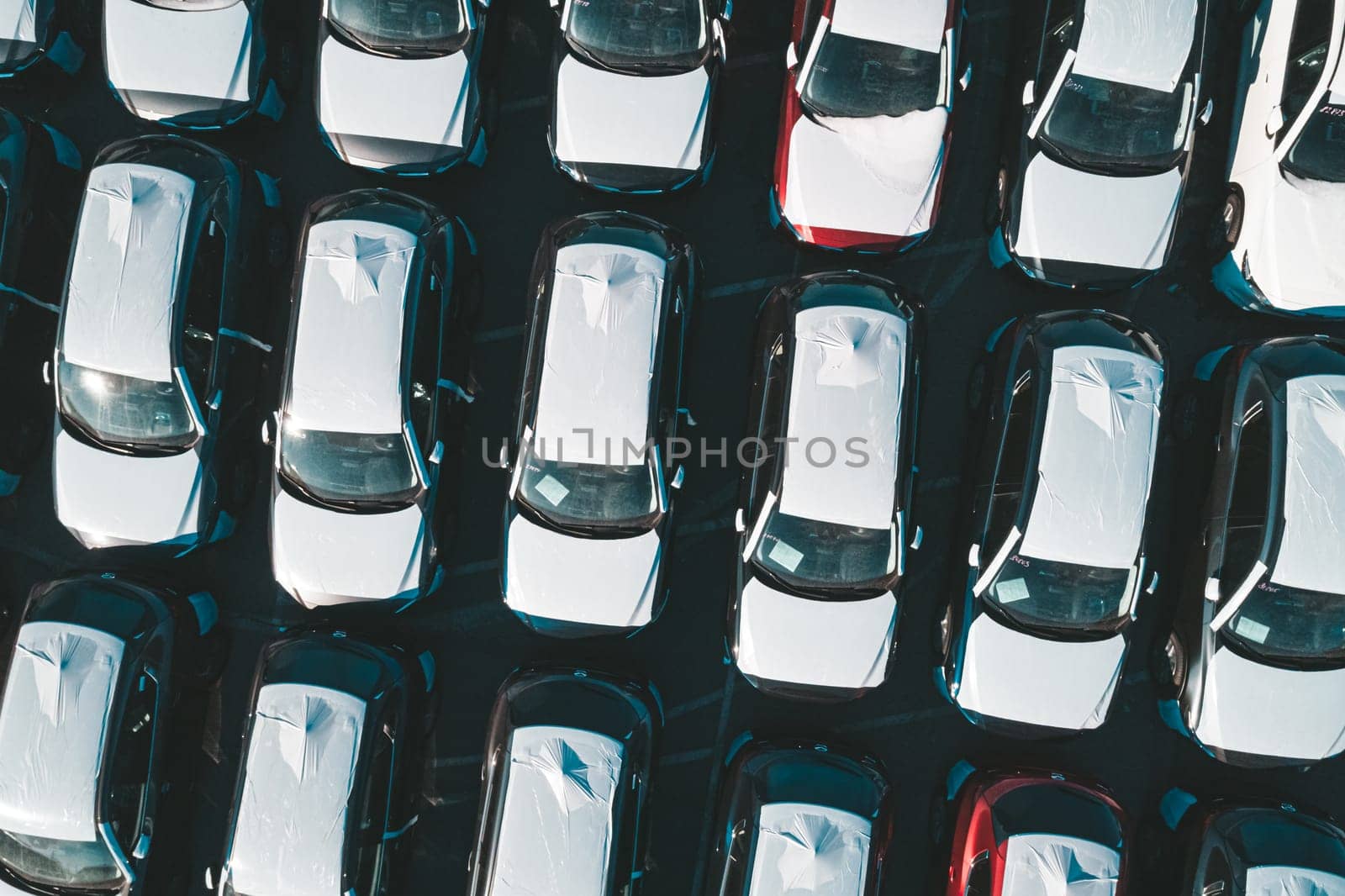 Aerial top down view of new cars parked in car parking lot. Car dealer parking lot full of new automobiles. New cars lined up for import and export business. by Busker