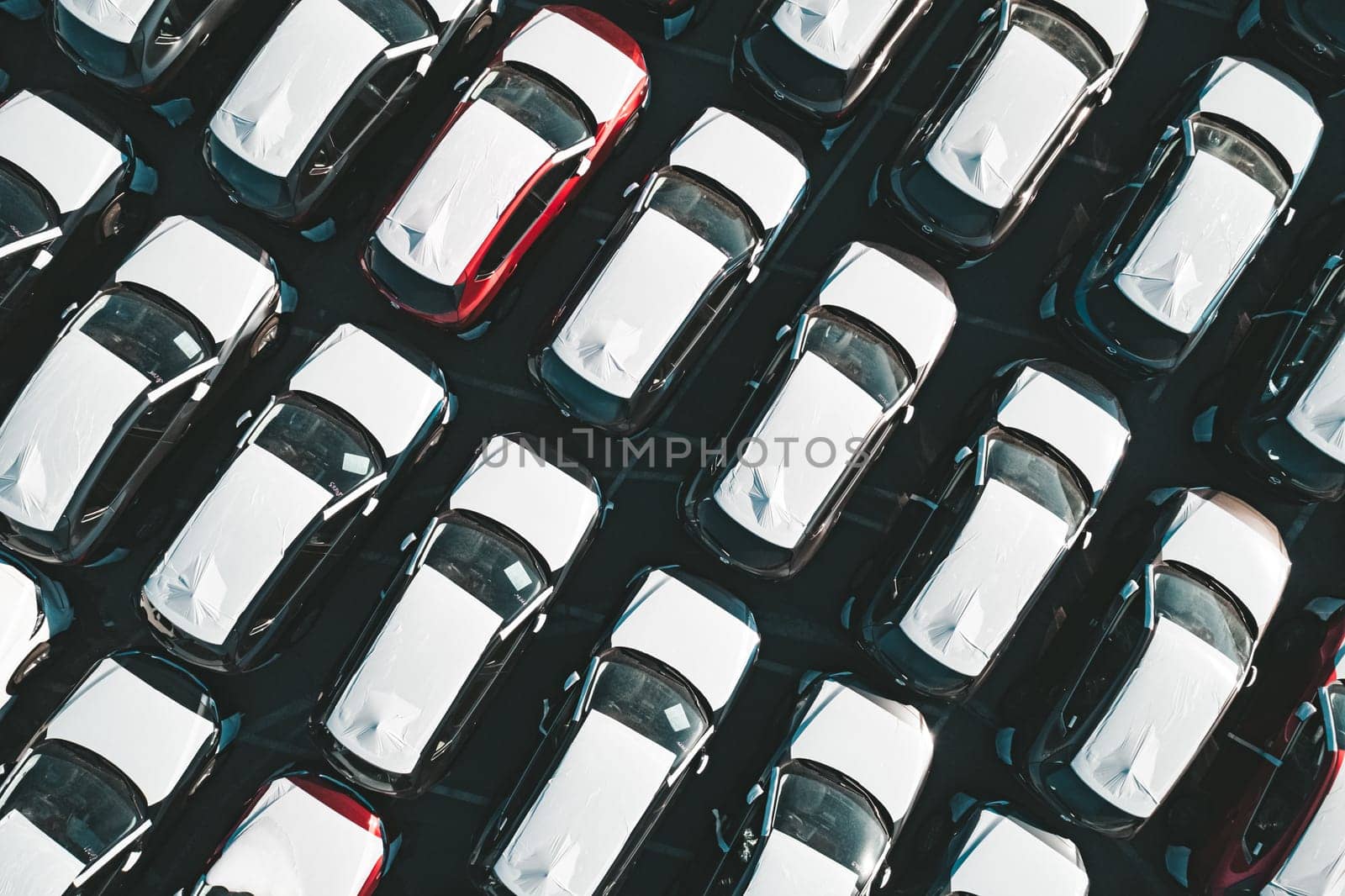 Aerial top down view of new cars parked in car parking lot. Car dealer parking lot full of new automobiles. New cars lined up for import and export business. by Busker